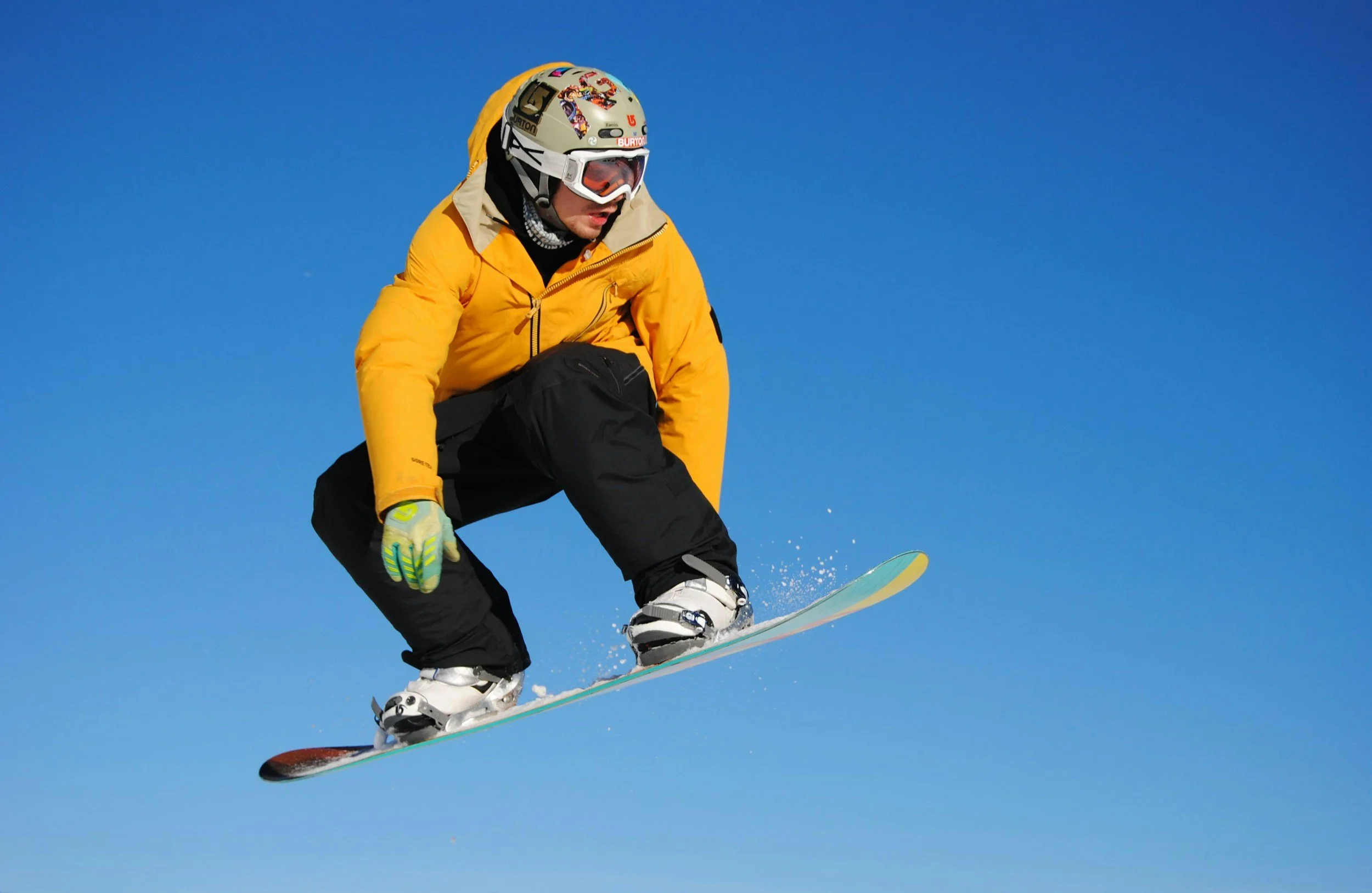 Snowboarder in a yellow jacket jumping against a clear blue sky