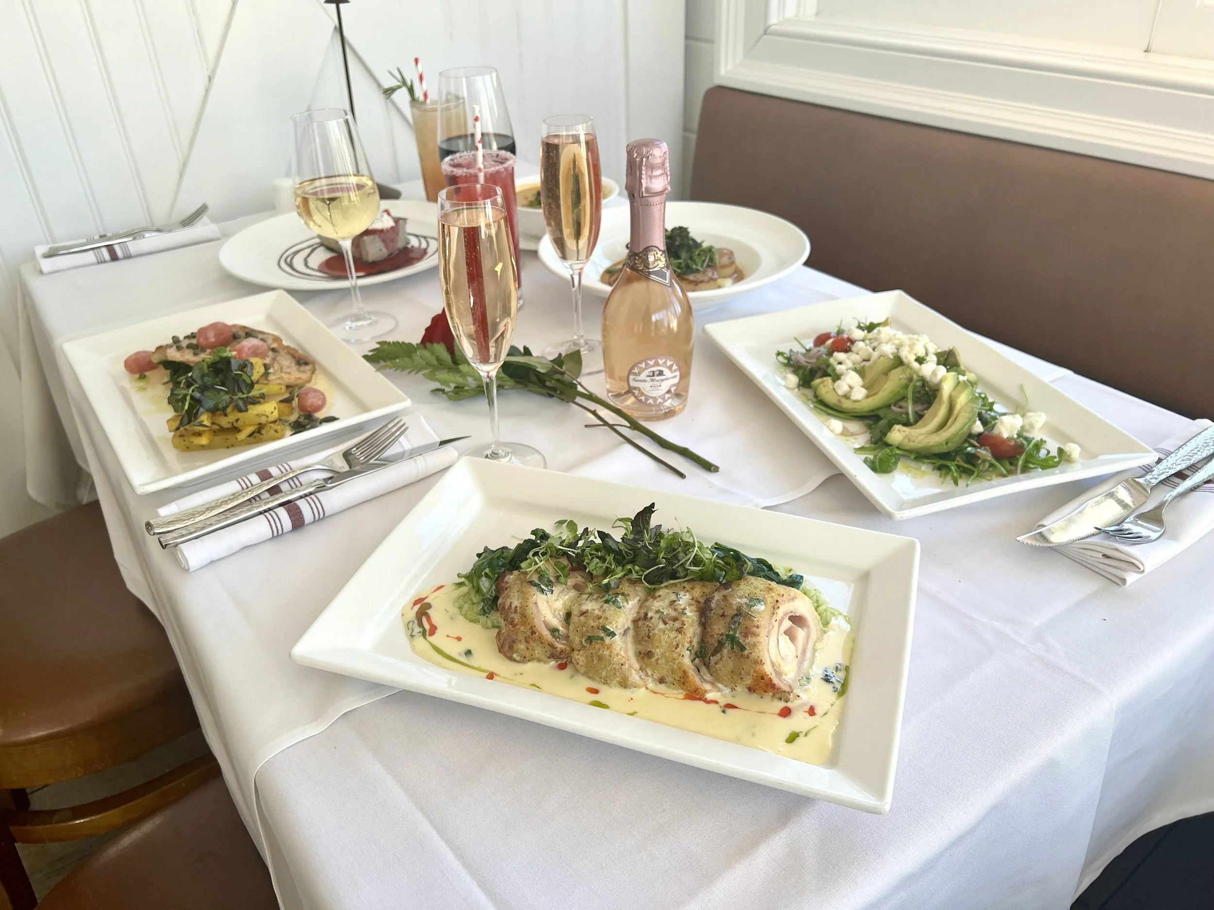 A three-course meal with a mixed green salad with toasted bread, a vegetable terrine with cucumber and edible flowers, and a beet and cheese salad with colorful vegetables, served on white dishes with a glass of red wine.