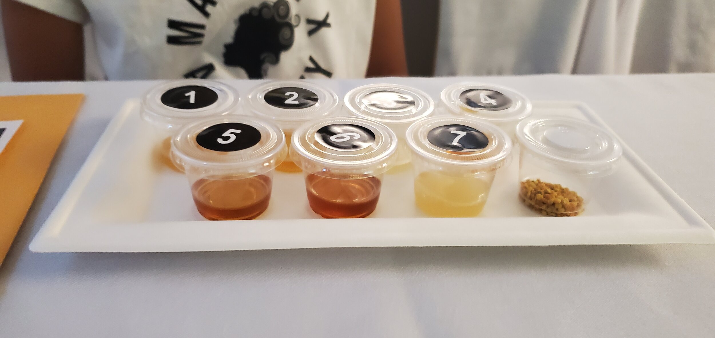 Small sample cups labeled 1 to 7, containing different colored liquids and a small amount of granules on a white tray.