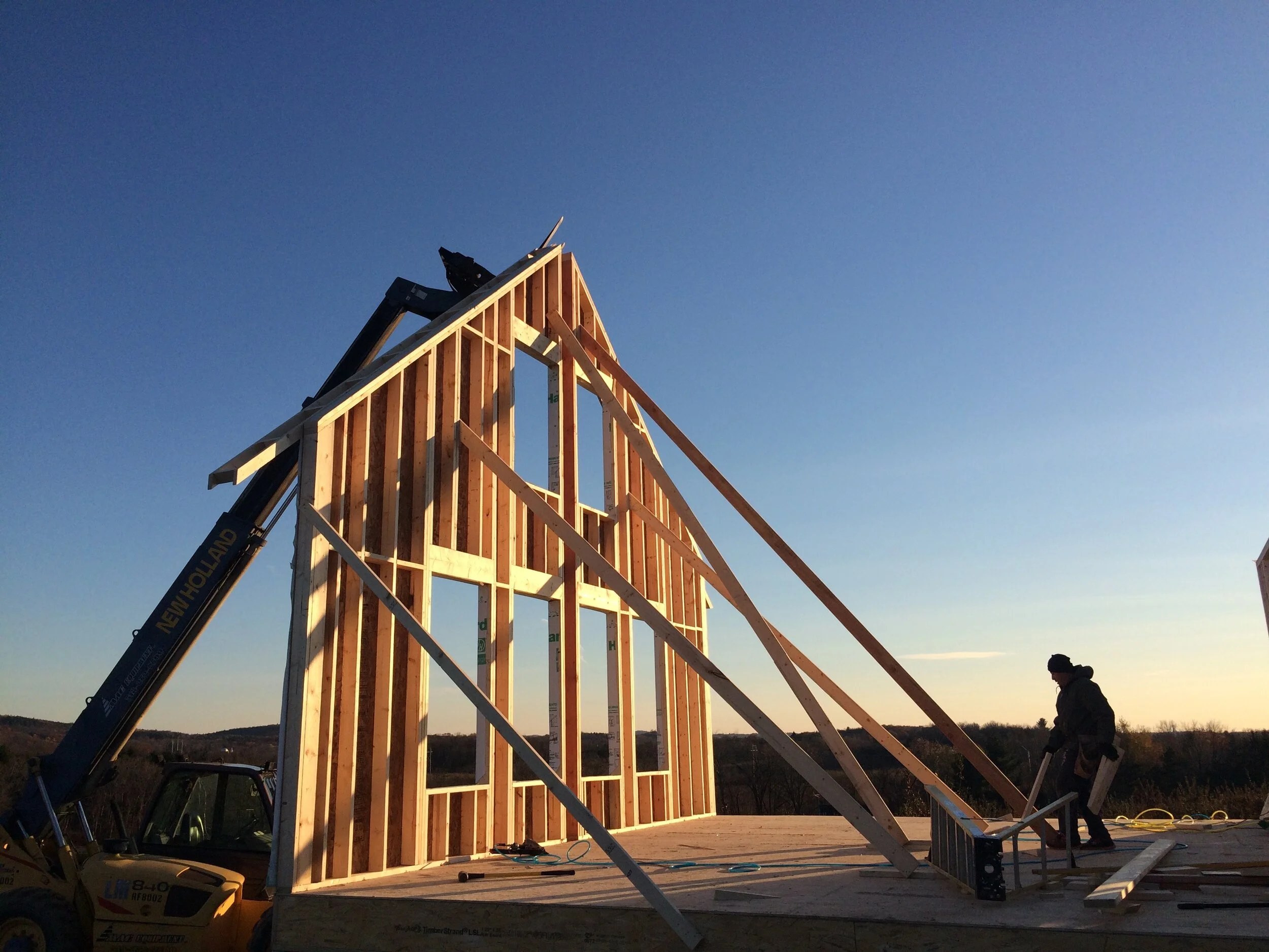 Construction worker framing a wooden structure on a building site during sunset.