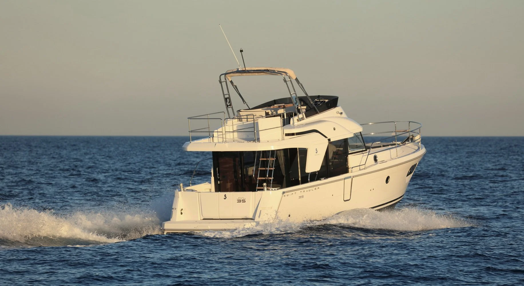 A Beneteau Swift Trawler 35 motor yacht sailing on calm blue ocean waters during sunset or sunrise.
