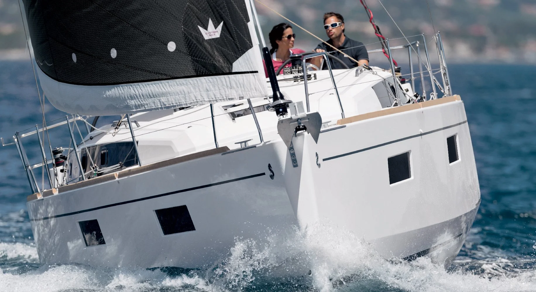Two people sailing on a Beneteau Oceanis 38.1 yacht with a black sail on blue water.