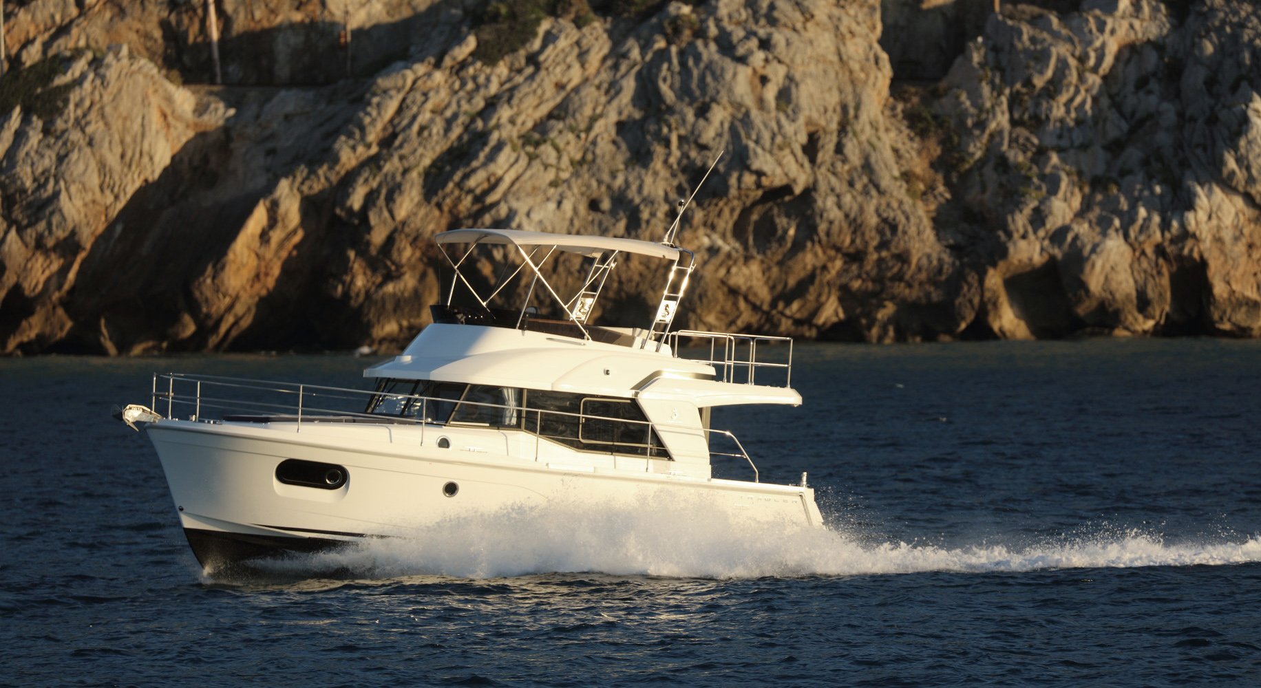 A Beneteau Swift Trawler 35 motor yacht cruising on the ocean near rocky cliffs.