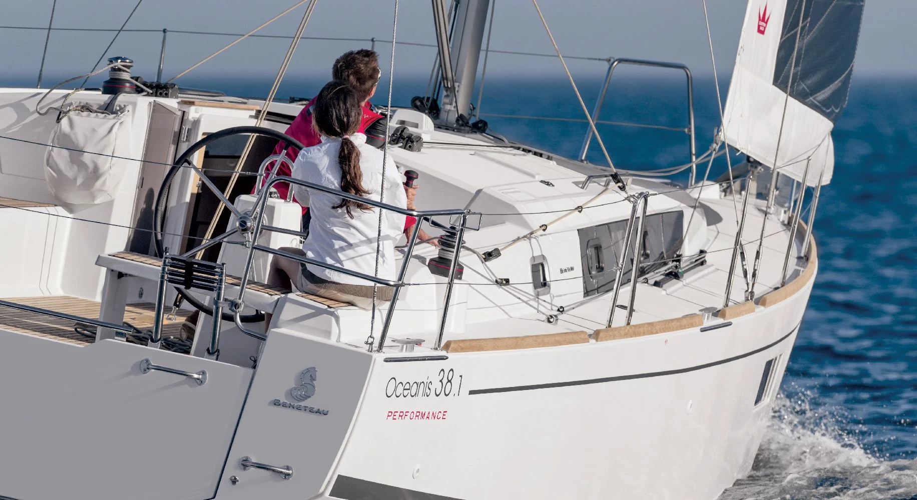Two people operating a white Beneteau Oceanis 38.1 sailboat on open water under a clear sky.