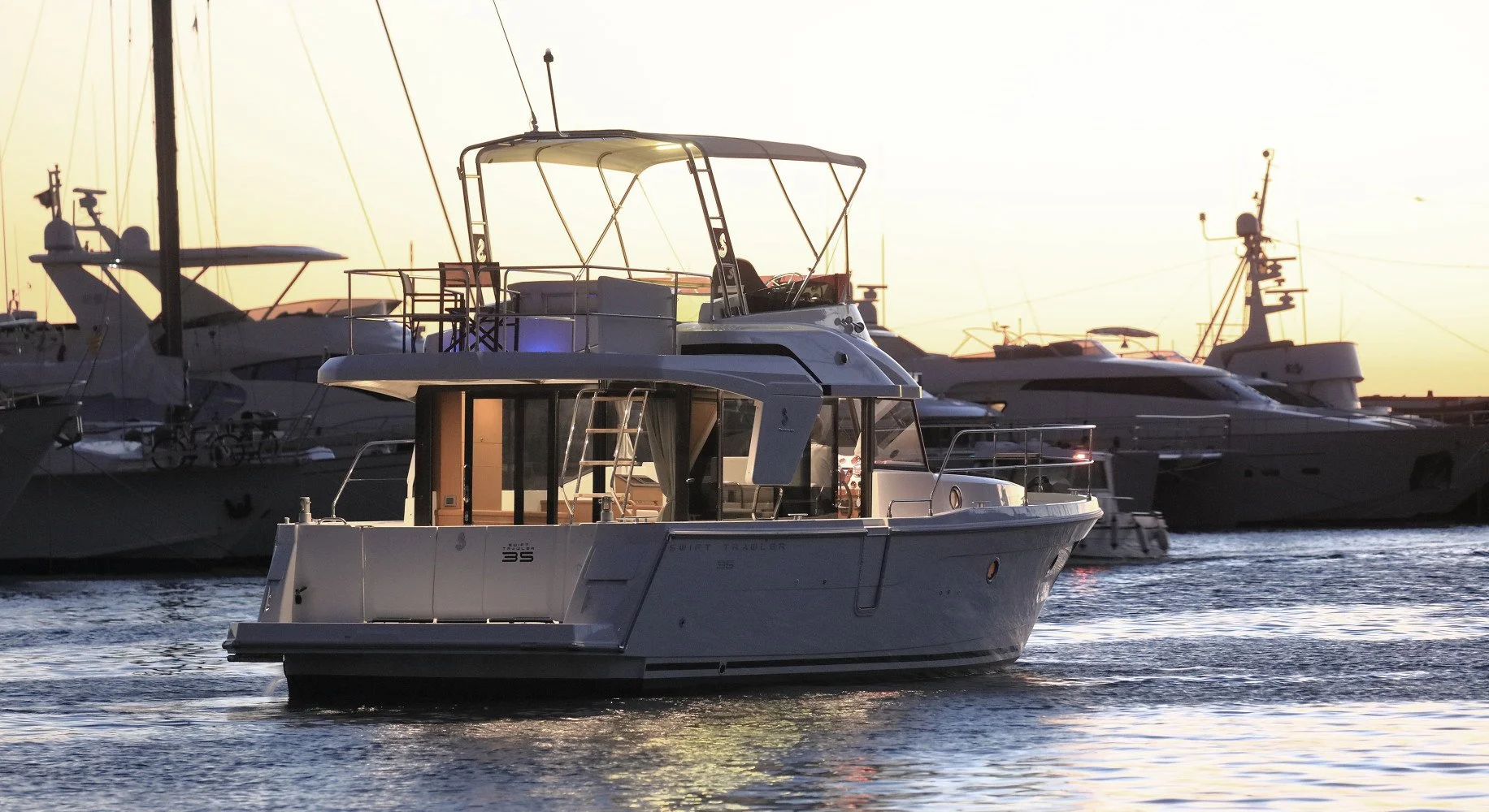 A Beneteau Swift Trawler 35 luxury motor yacht sailing in a marina with other yachts at sunset.
