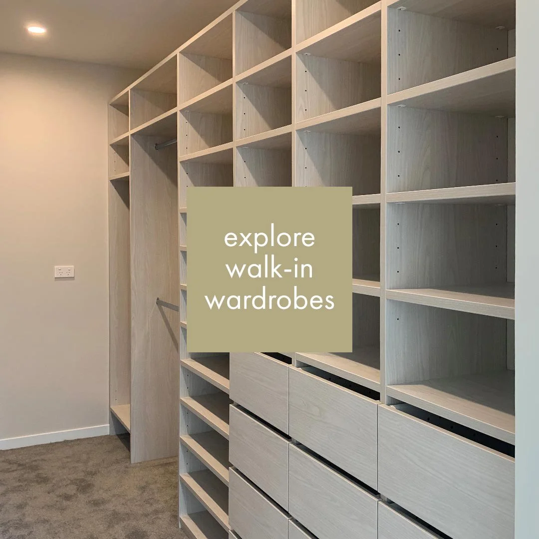 Empty walk-in wardrobe with wooden shelves and drawers, beige walls, and carpeted floor.