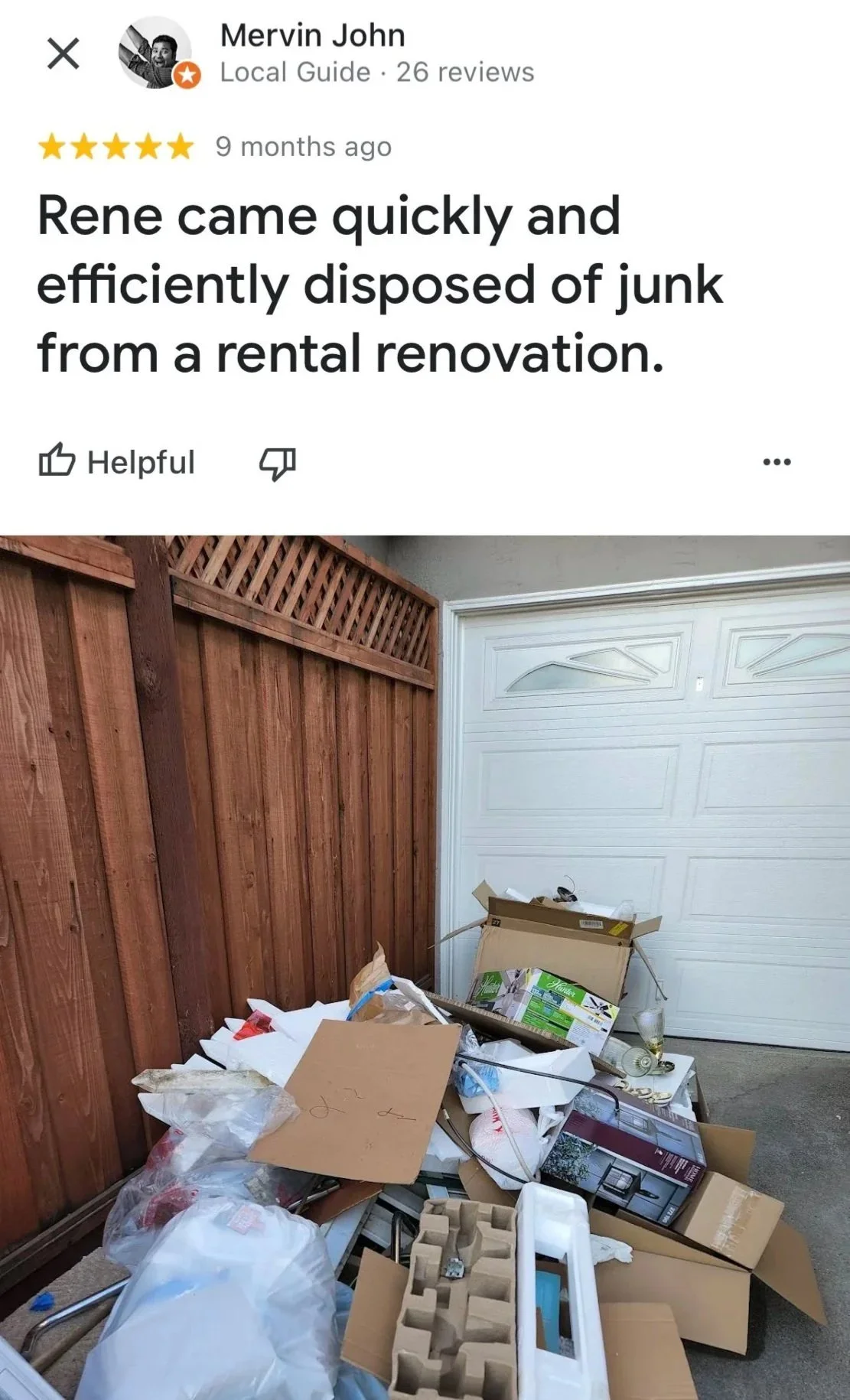 A pile of trash and discarded boxes in a garage next to a wooden fence.
