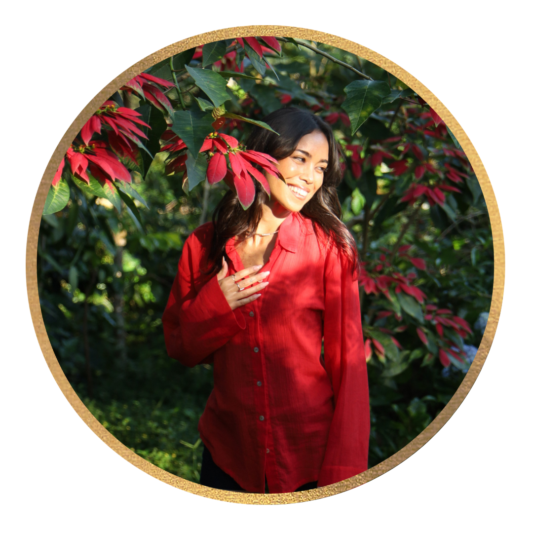 A woman wearing a red shirt smiling outdoors among red and green foliage.