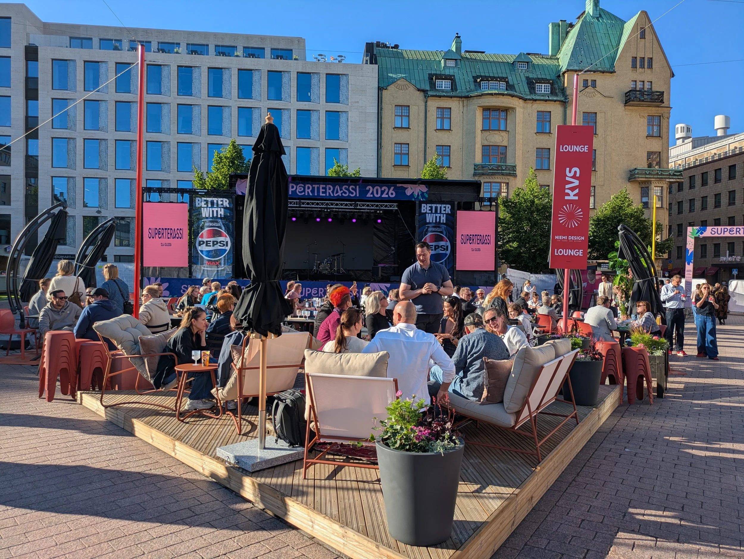 The photo shows happy people at Superterassi. In the foreground is the KVS lounge, and in the background are more people and the Superterassi stage, decorated with Pepsi logos.