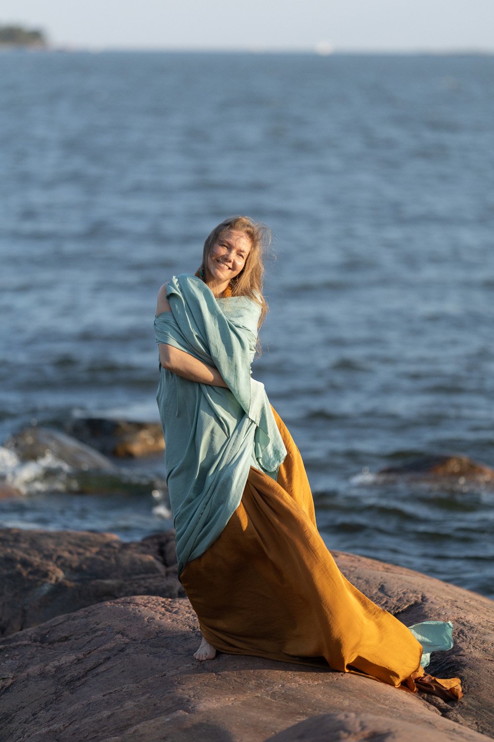 Anni Pellikka smiling by the sea, wrapped in a light blue fabric.