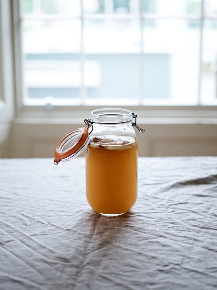 Jar of homemade kombucha on a table by a window.