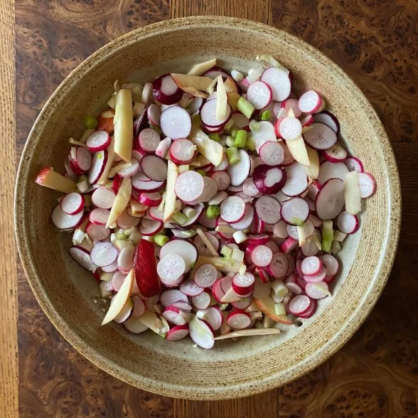 Bowl of sliced fermented radish with apple and spring onion.