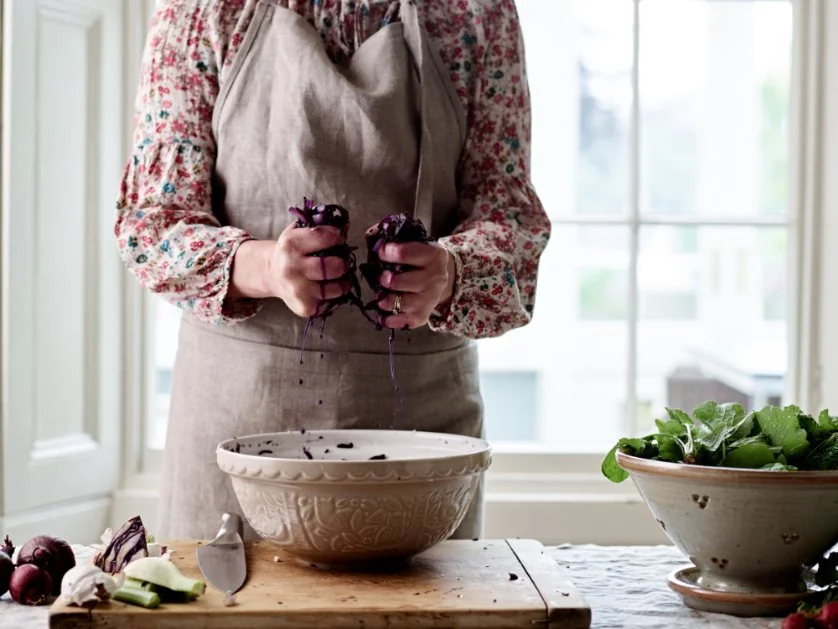 Hands squeezing shredded red cabbage over a bowl to test moisture for sauerkraut.
