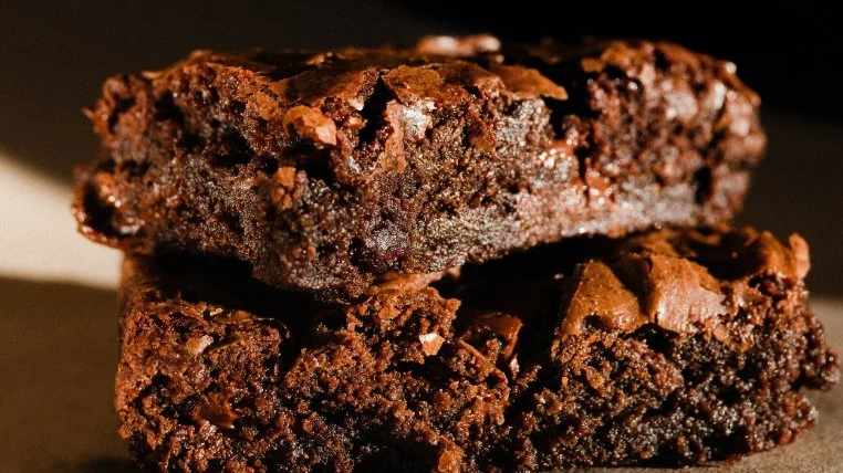Close-up of two stacked chocolate brownies with a crackled top.