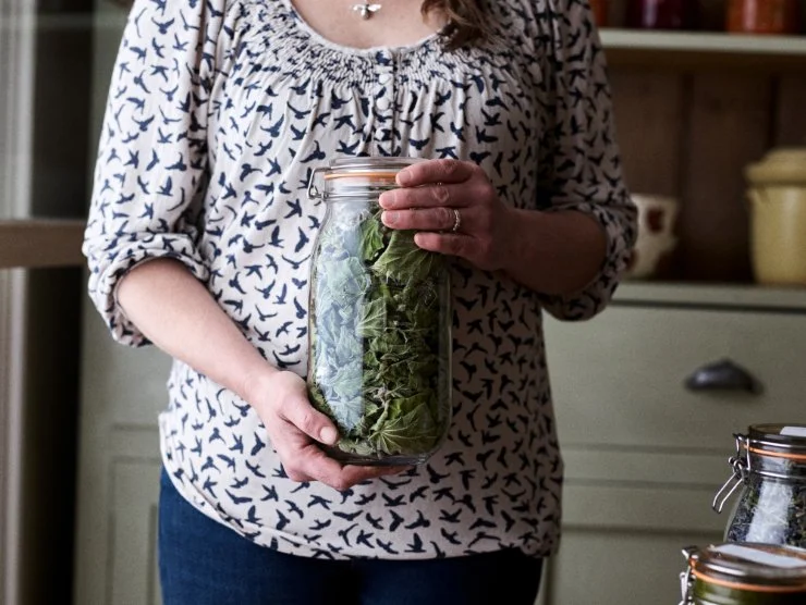 Jo holding a large jar filled with dried marshmallow leaves.
