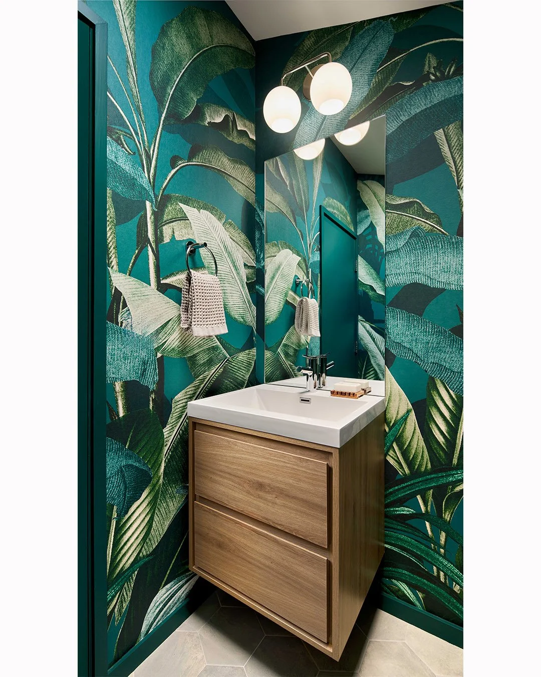 Bold pattern and simple detailing bring energy to a compact space. A floating vanity and globe sconces keep things minimal, while botanical wallpaper wraps the room in color and texture. 🌴🌿

Builder: @starburst.construction 
📸 @cesarrubiophotograp