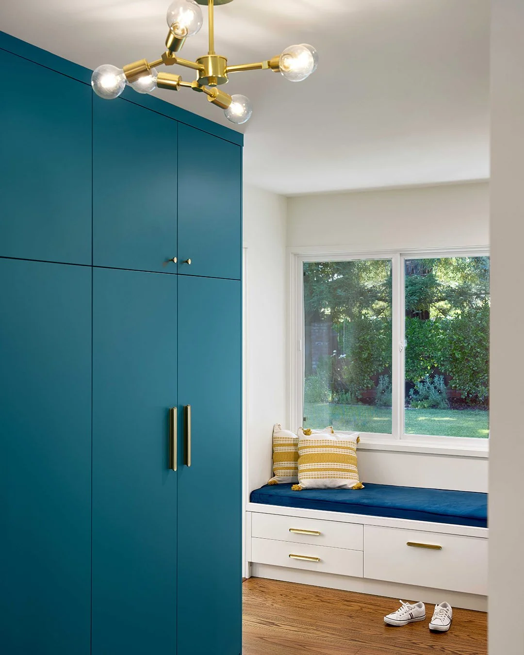 Bright, painted millwork defines the new entry of this Menlo Park home, a functional threshold lined with storage, seating, and daylight. Brass details and a sculptural fixture add subtle contrast to the saturated palette. 

Builder: @starburst.const