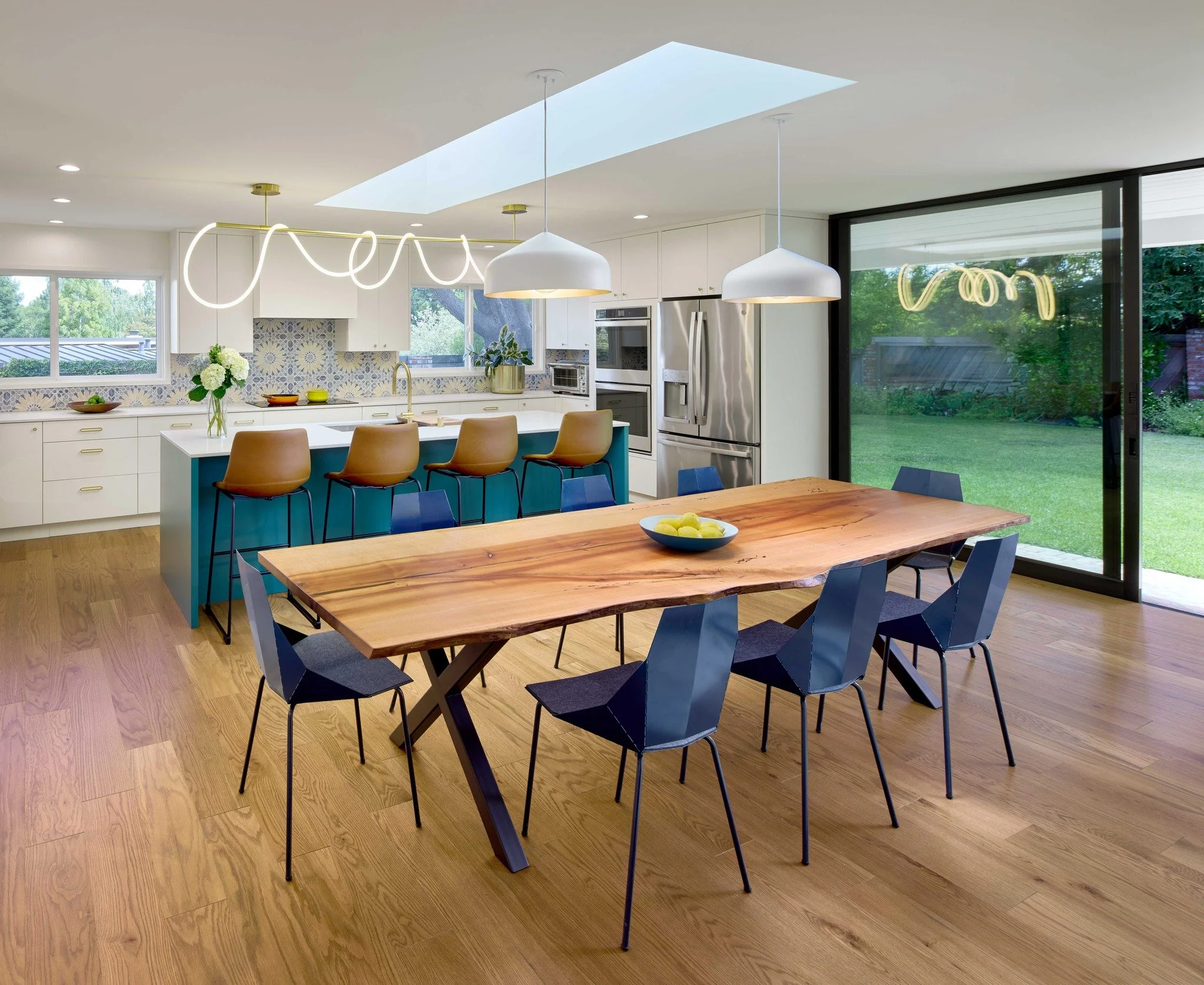 A bold new island in custom color anchors this recently renovated kitchen, paired with bright white cabinets and a lively, patterned tile backsplash. The design opens up the kitchen and dining space to improve flow and creates a cheerful gathering sp