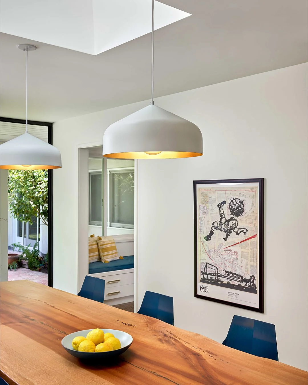A skylight placed just above the live-edge dining table brings daylight to the center of the room. Matte white pendants with brushed gold interiors add a warm glow, setting the tone for everyday meals and easy gatherings. Bold art brings its own stor