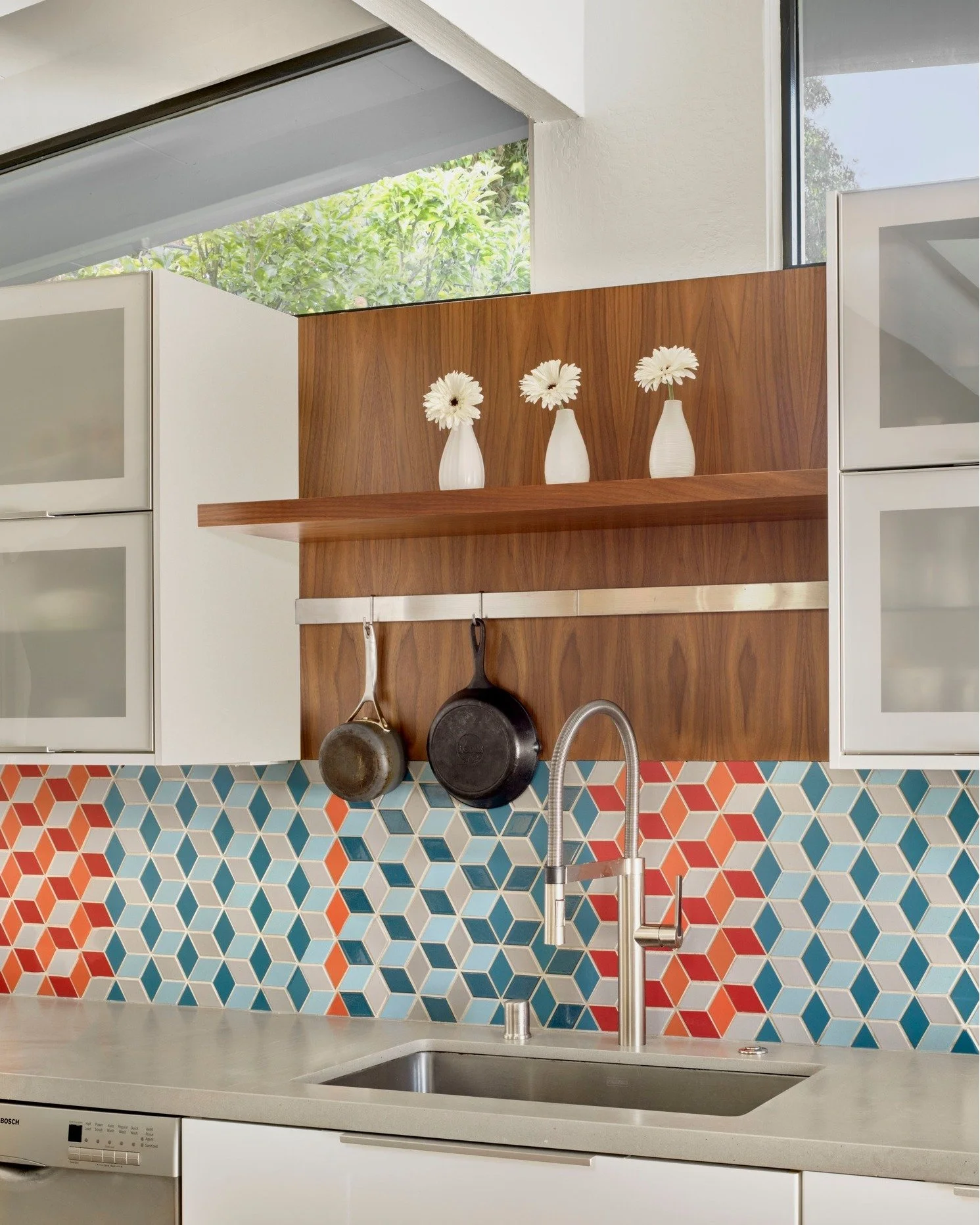 By removing a central divider in this typical California ranch-style home, this modest footprint opens up to light, air, and flexibility. A reoriented kitchen, featuring crisp, white cabinets, colorful mosaic tiles, and walnut accents, anchors the sp