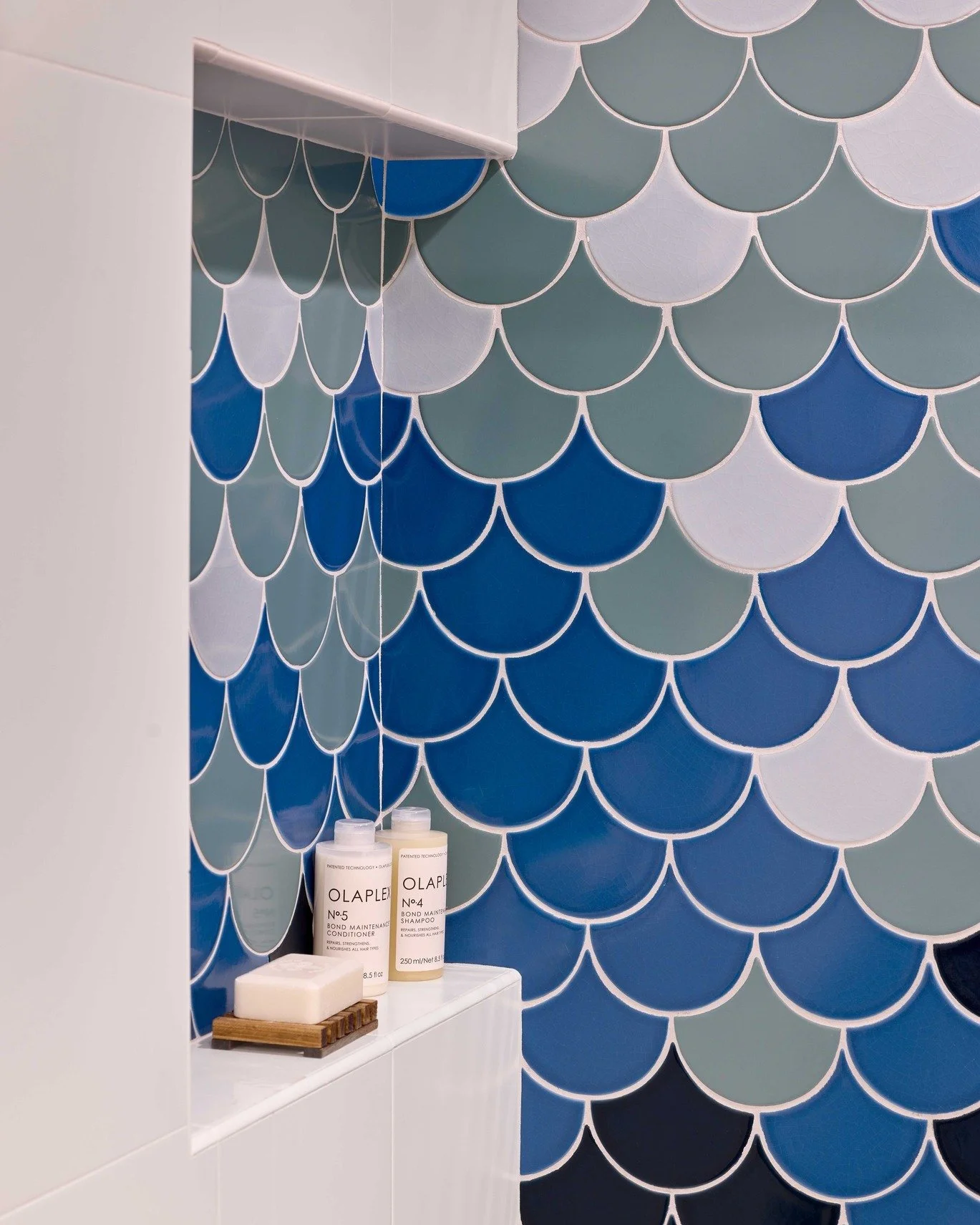 Two spaces, same idea: let the tile lead. In the bath, scalloped blues wrap the niche and shower, shifting tone from teal to navy. In the kitchen, a patterned backsplash turns a clean white cabinet wall into a focal point. Minimal hardware and lines 