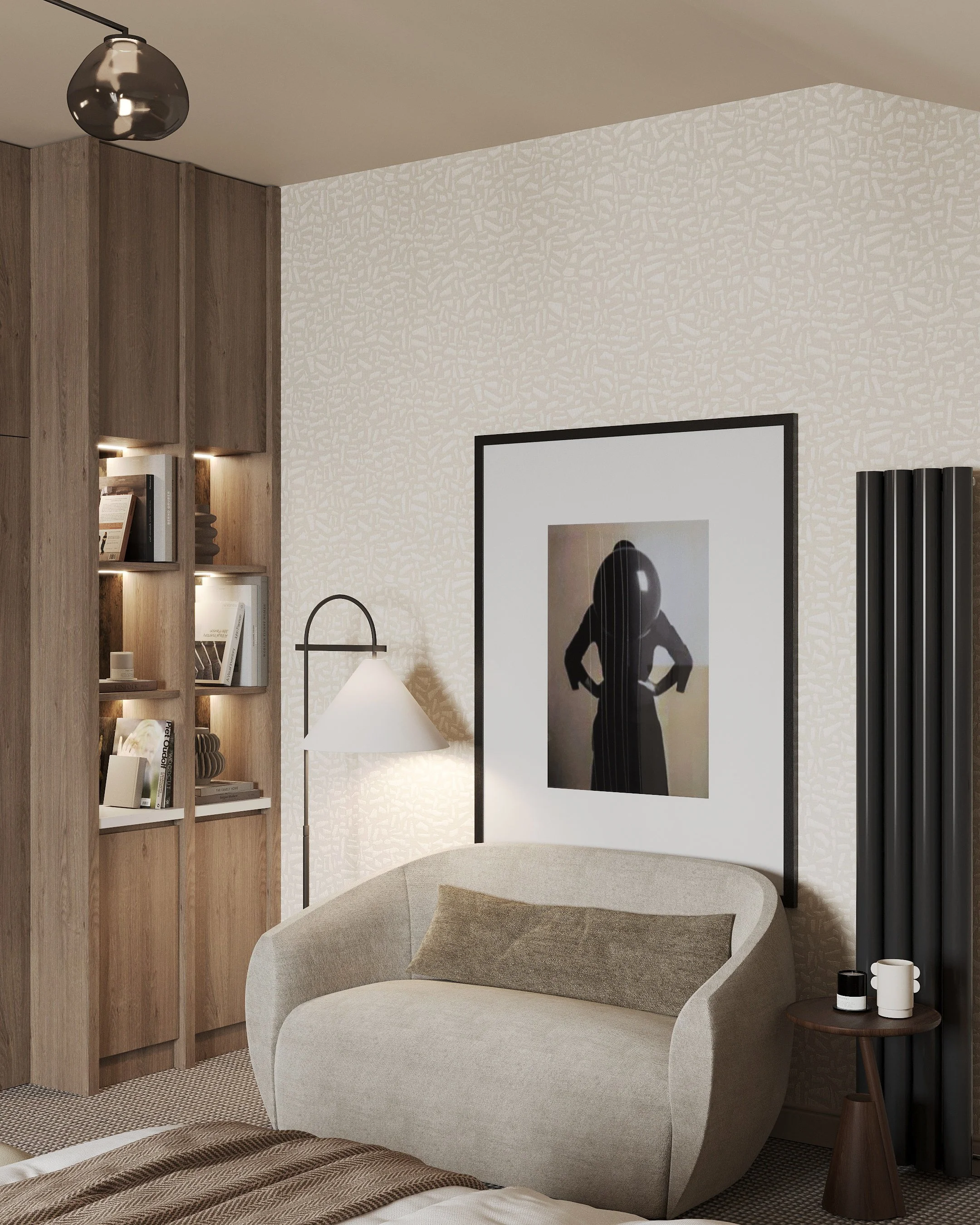 A cozy living room corner with a beige curved sofa, a framed abstract silhouette photograph of a woman, a black vertical radiator, a small wooden side table with two mugs and a candle, a white floor lamp, and a built-in wooden bookshelf with decorati