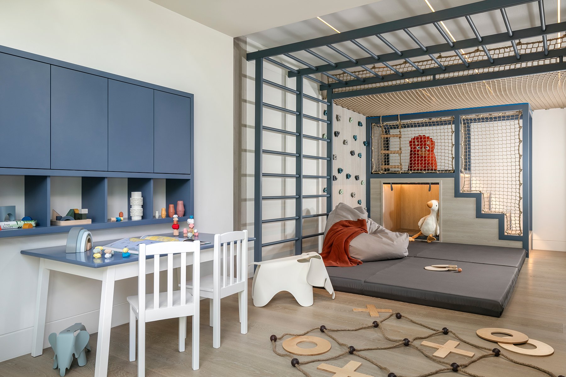 Child's playroom with a climbing wall, a cushioned area with a stuffed animal, a small table with chairs, and toys.