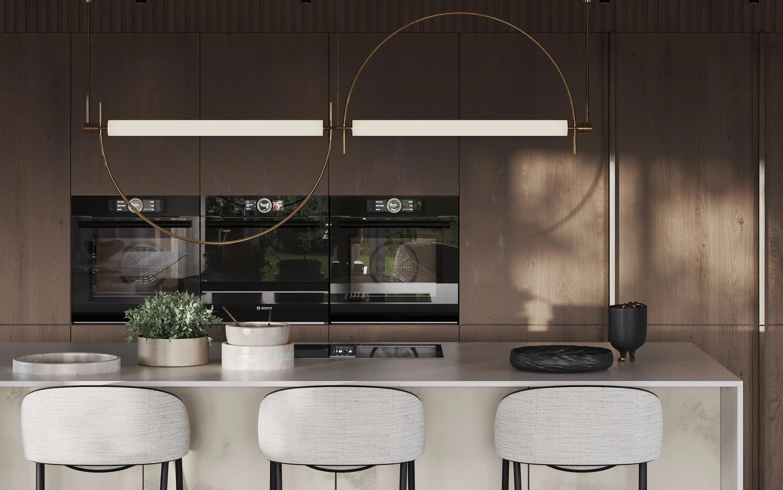Modern kitchen interior with dark wooden cabinets, built-in ovens, a white island with three white fabric chairs, and minimalistic decorative items, including a black vase and trays, a potted plant, and a black sculptural dish, illuminated by a conte