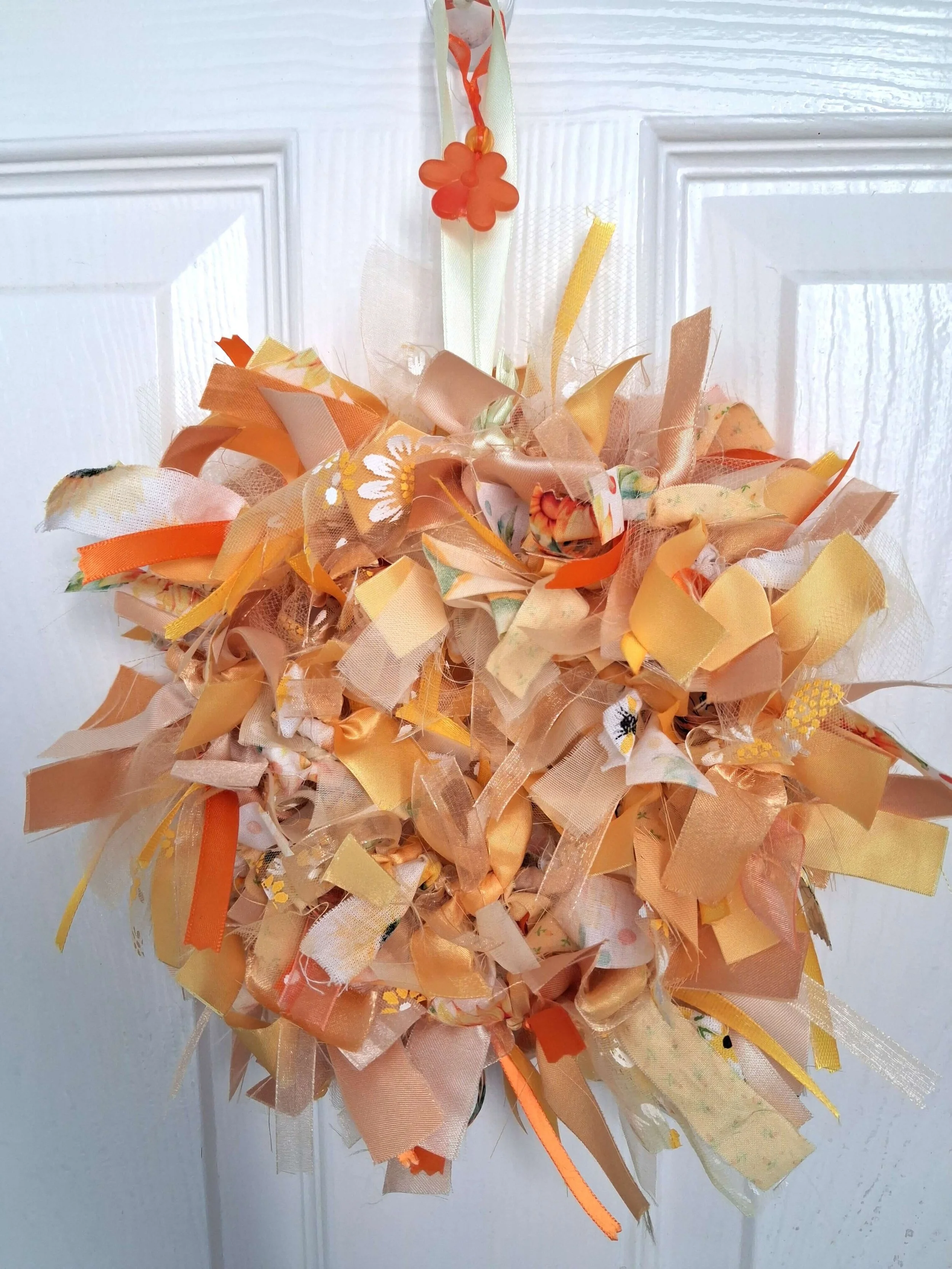 Decorative hanging ornament made of orange, peach, and yellow fabric and ribbons