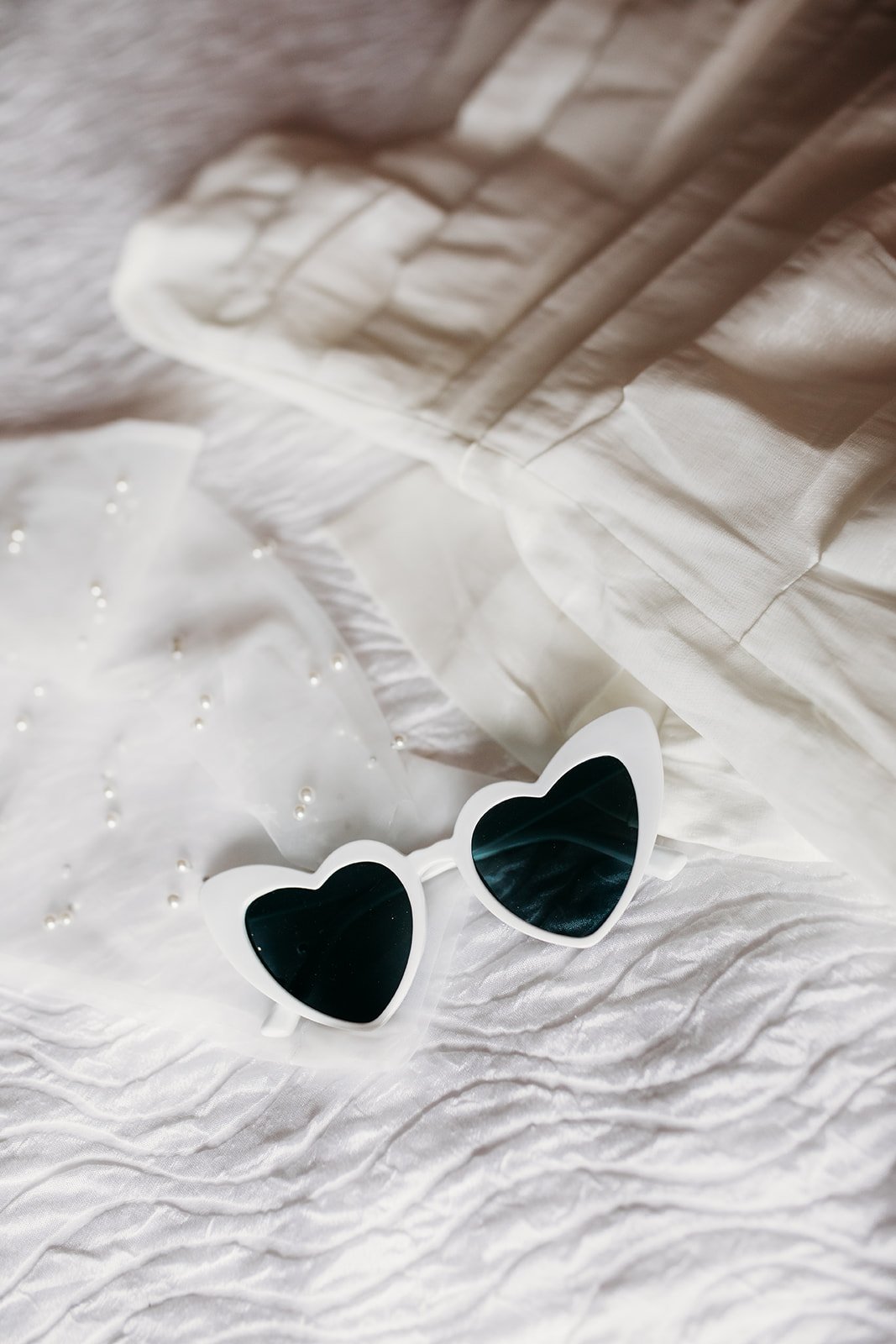 white heart shaped sunglasses rest on white bed