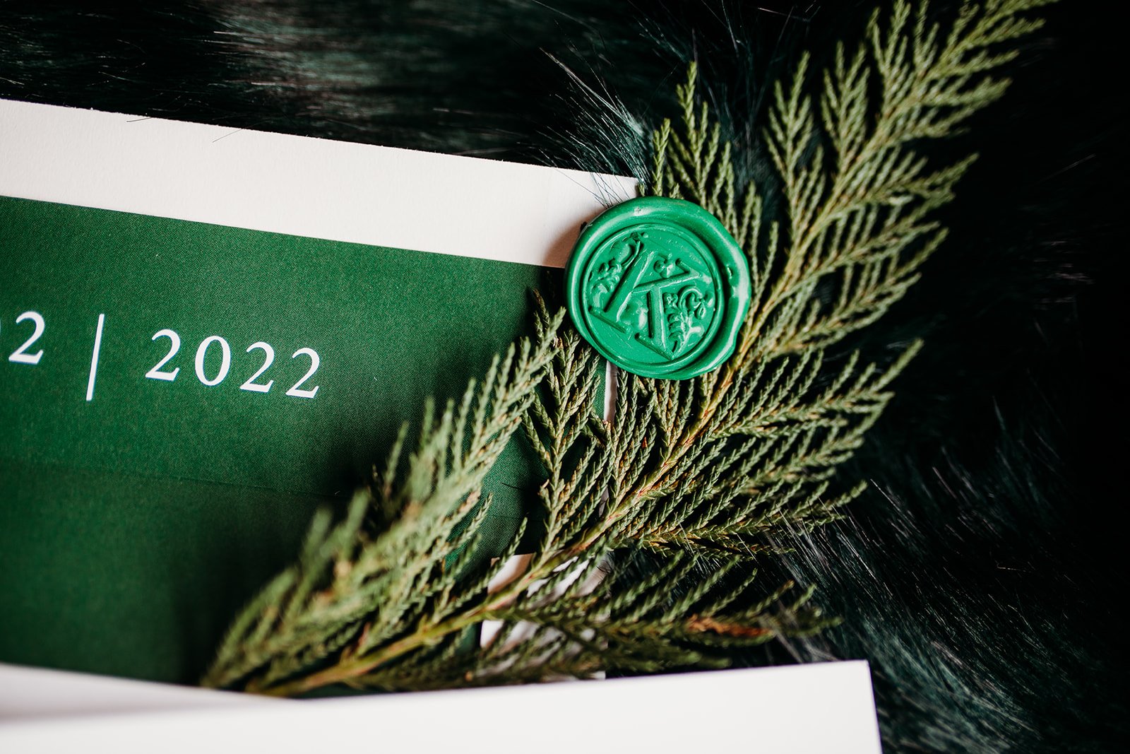 green wax seal with K lays on pine greenery