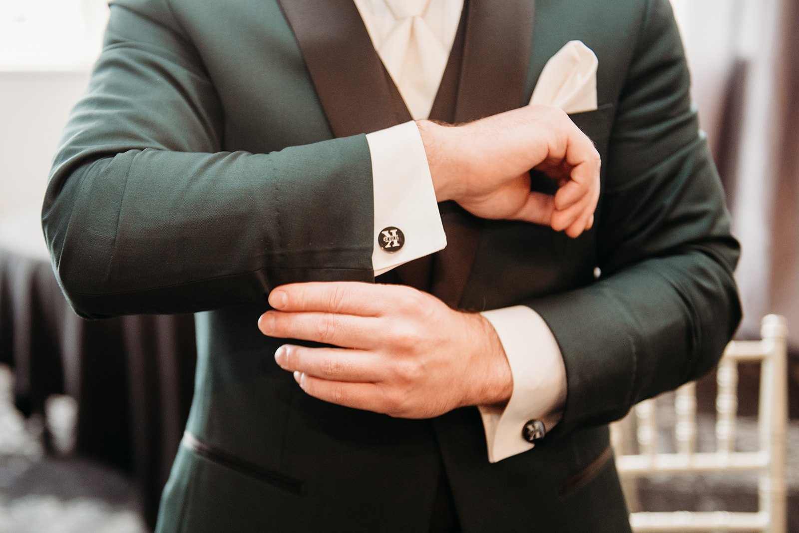 groom adjusts cufflinks on emerald green suit for winter wedding