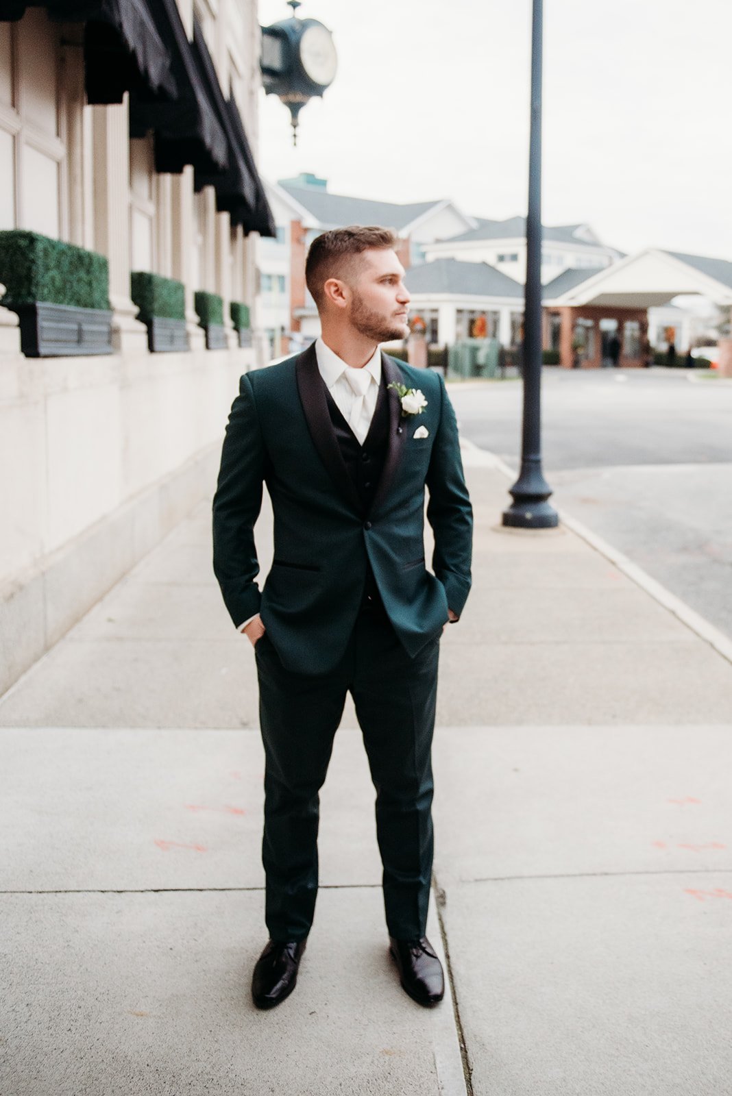 groom stands with hands in pocket wearing emerald suit jacket