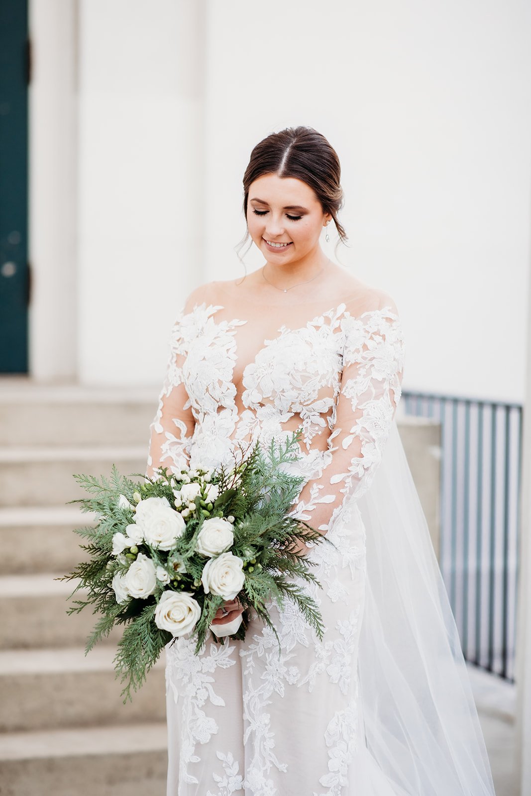 bride looks down at white bouquet in wedding gown with lace sleeves