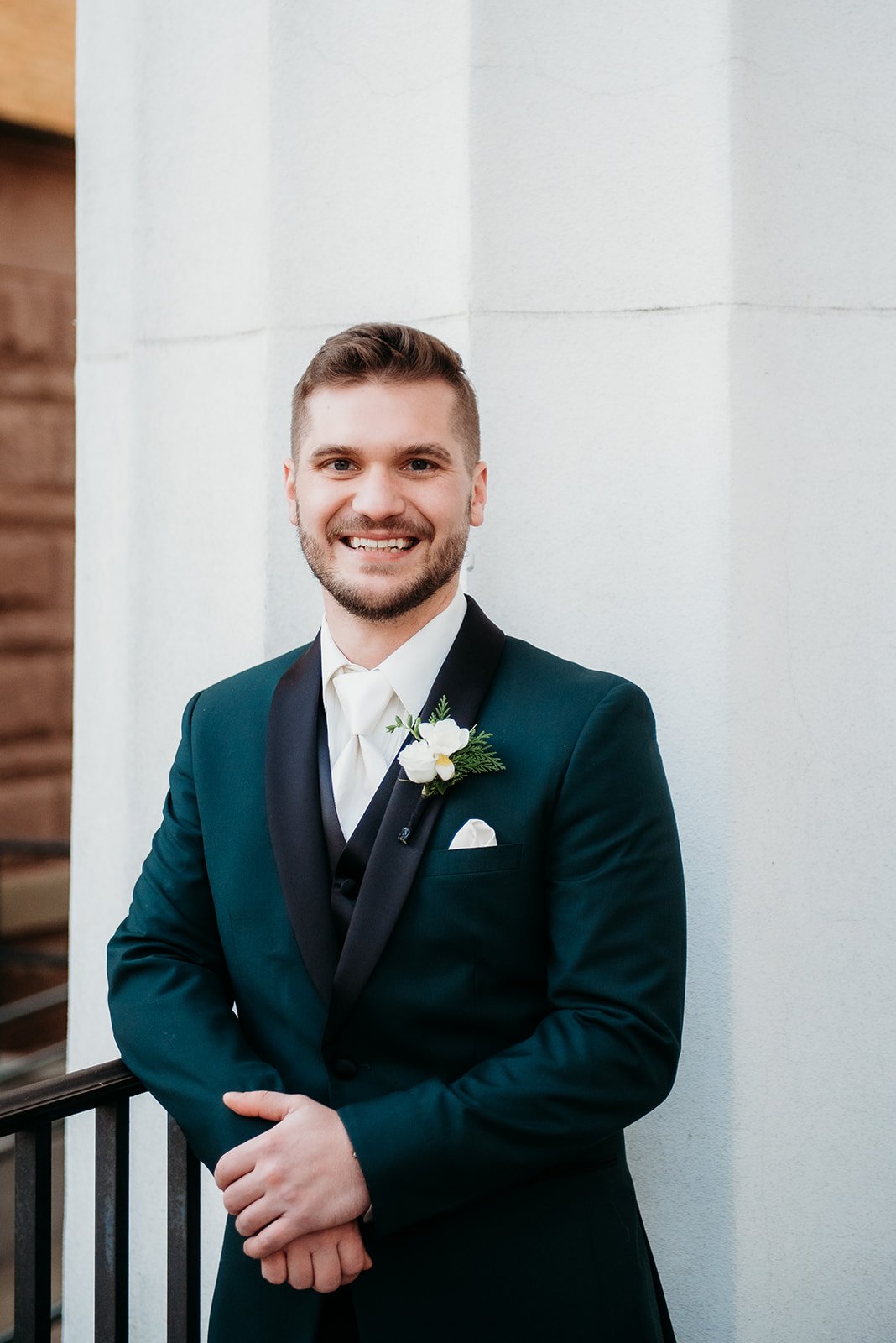 groom leans on banister in emerald jacket