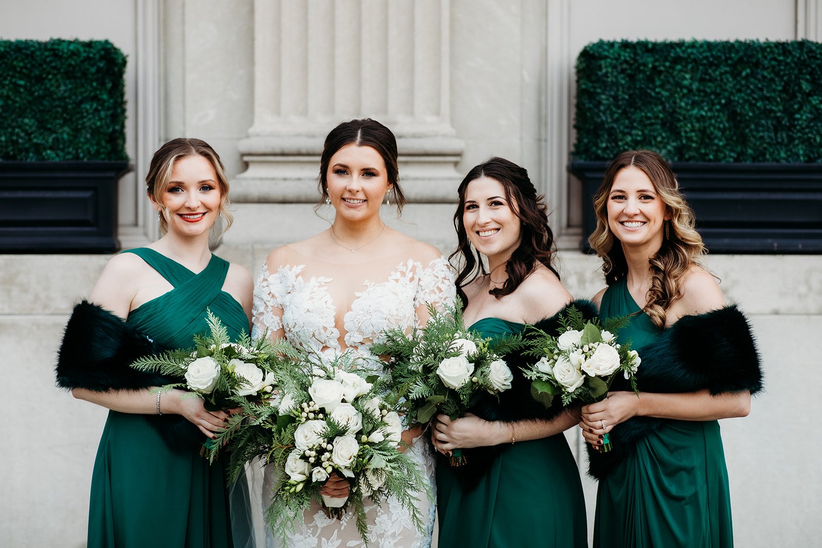 bride poses with bridesmaids in emerald green gowns for winter wedding