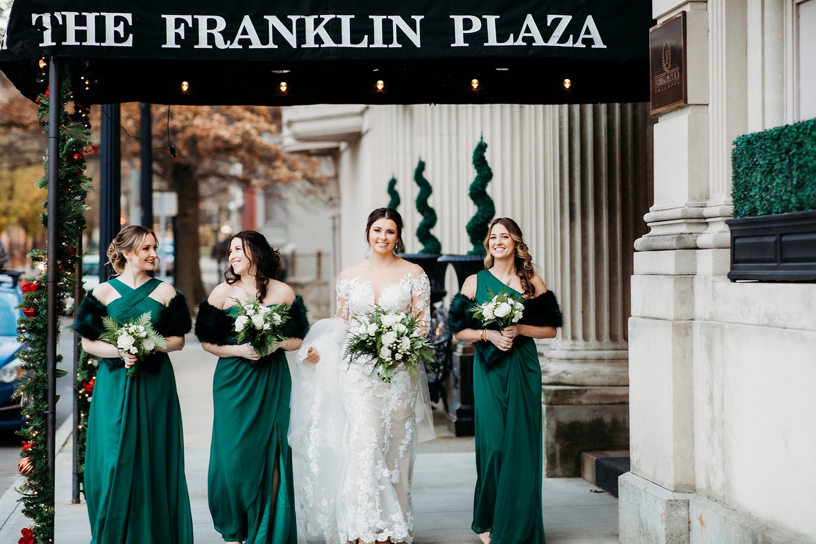 bride stands with bridesmaids in emerald gowns under sign by the Franklin Plaza in Troy NY