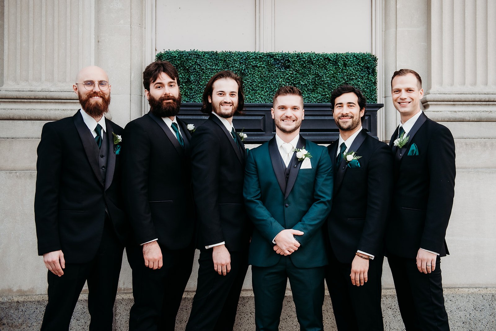 groom stands with groomsmen in emerald suit jackets