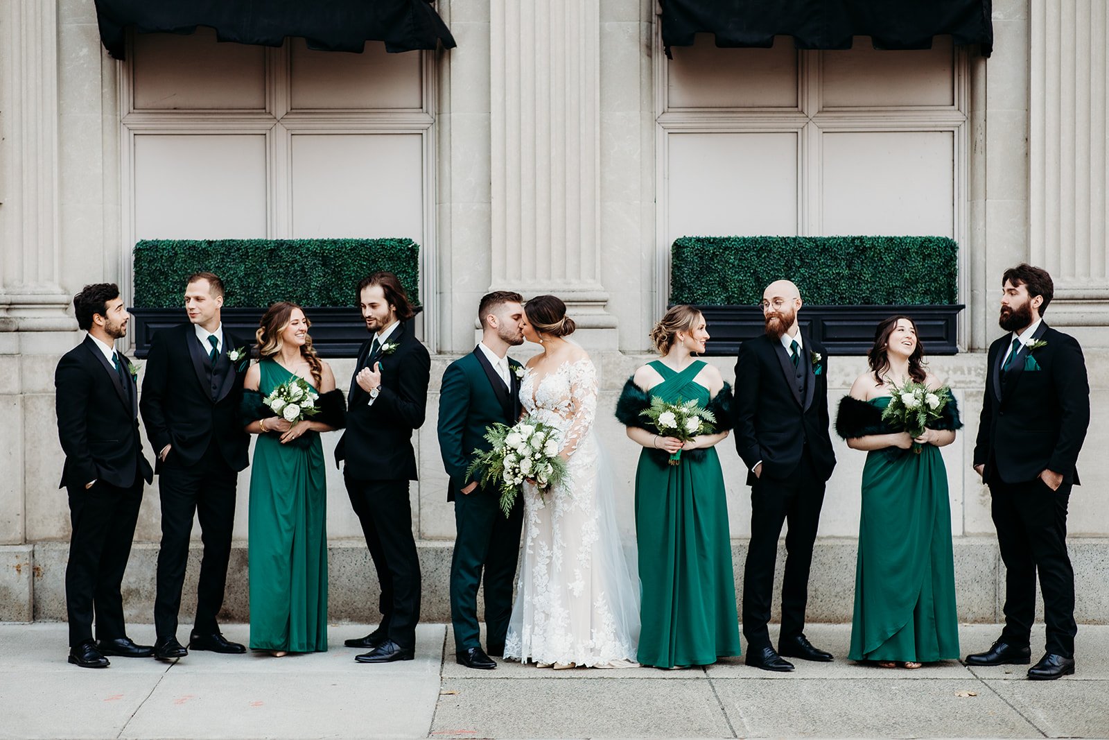 bride and groom kiss with wedding party in green and black around them by the Franklin Plaza in Troy NY