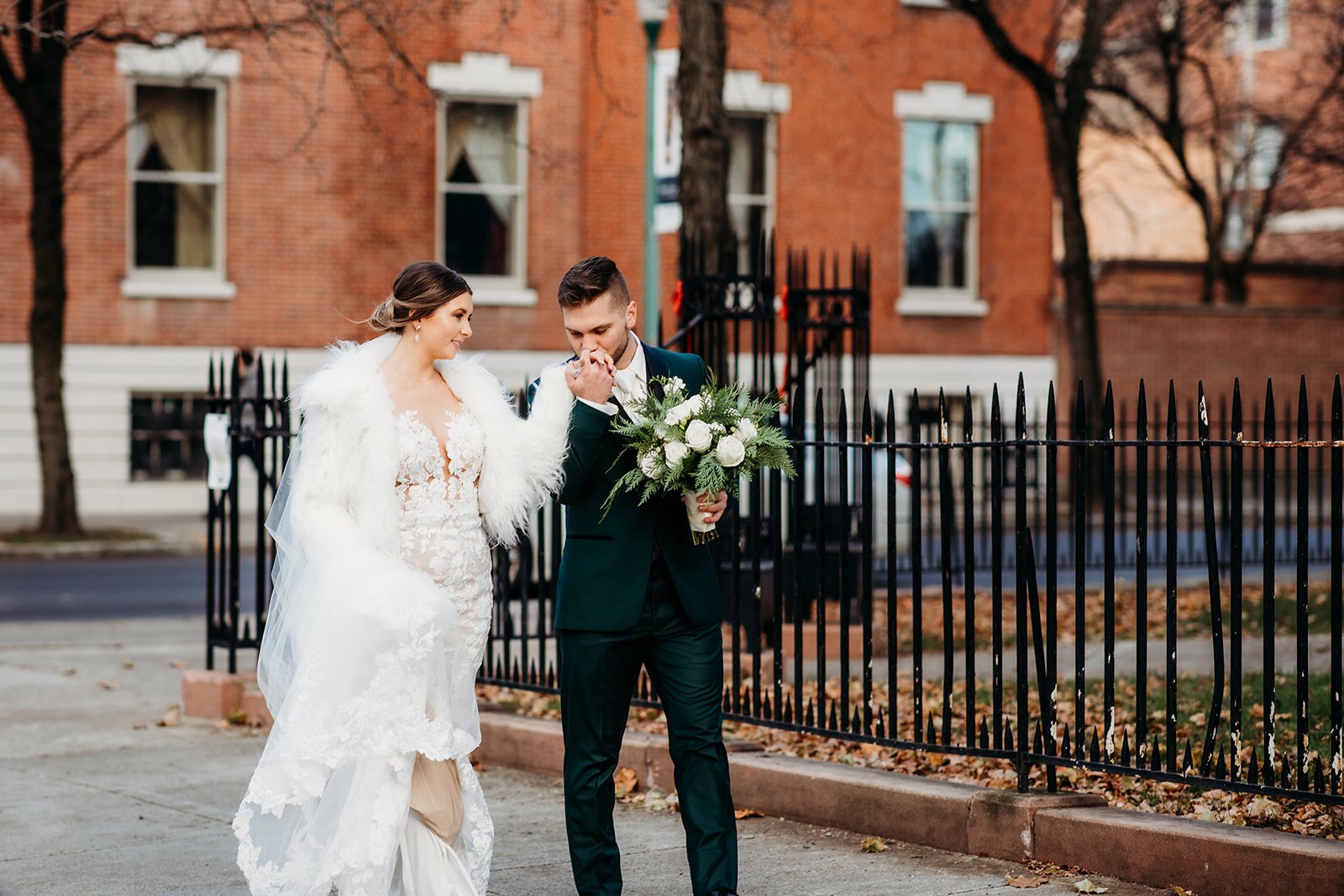 bride and groom hold hands walking down sidewalk in Troy NY while groom kisses bride's hand