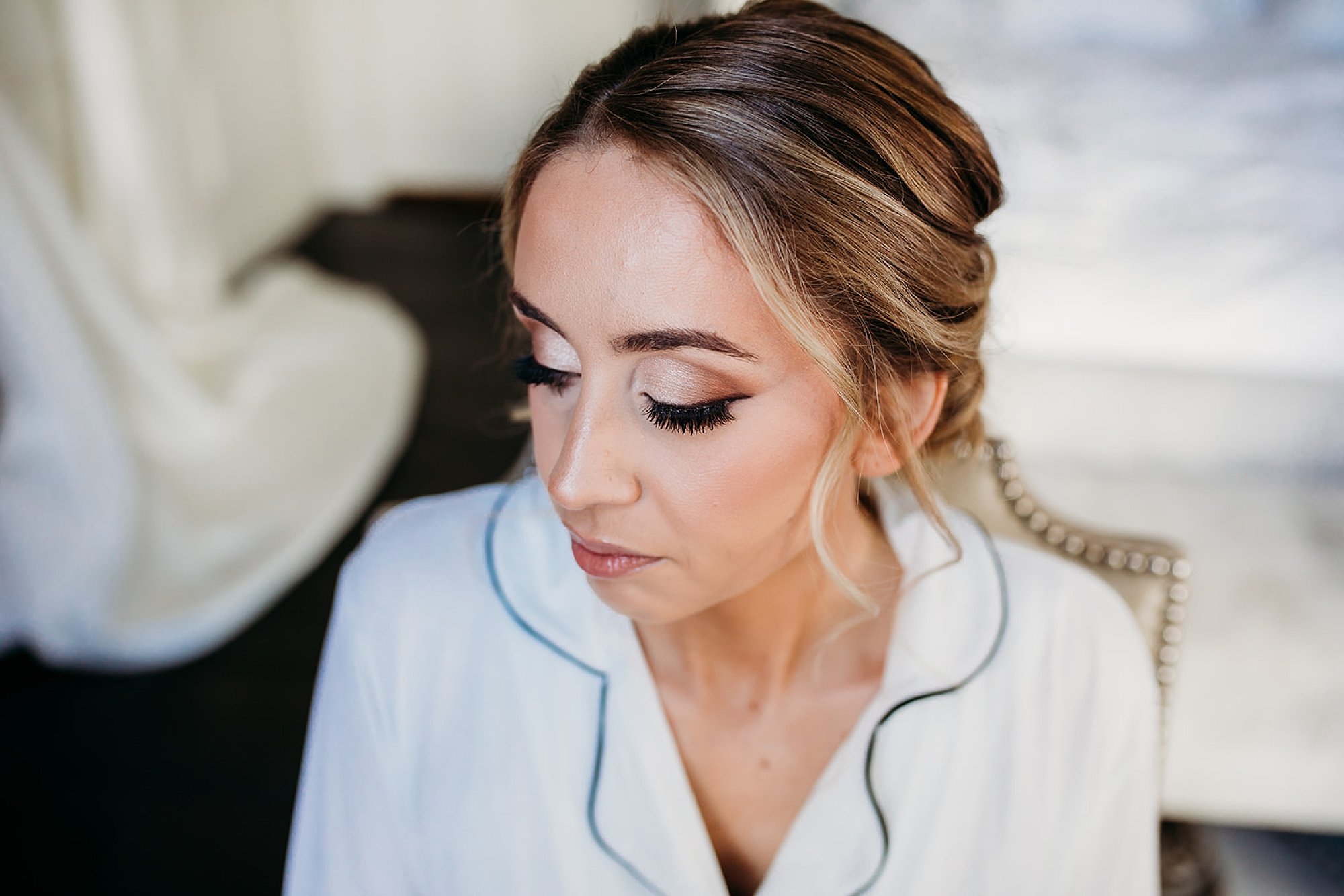 bride in white pajamas looks down showing off eye shadow 