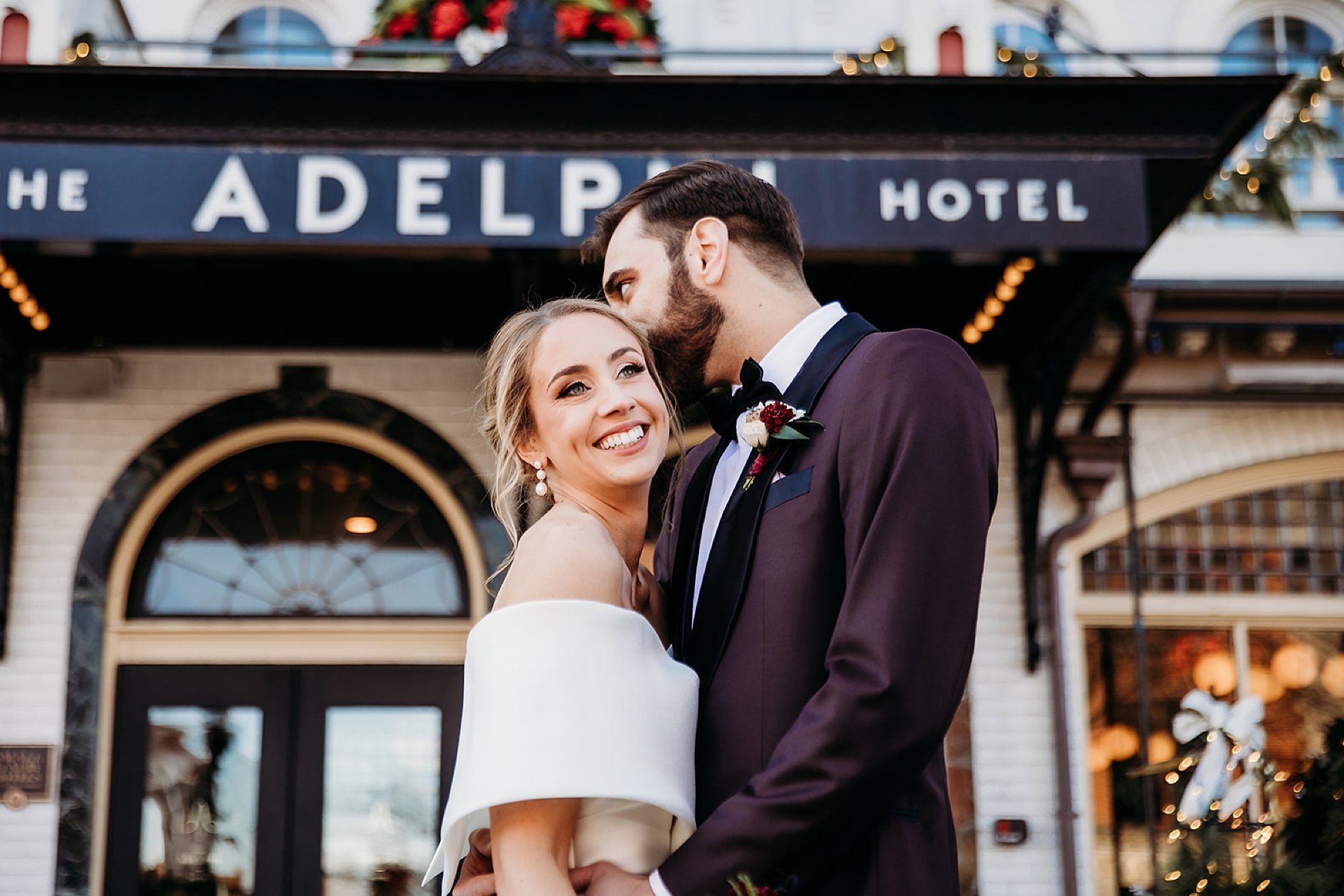groom in burgundy jacket kisses bride's forehead outside The Adelphi Hotel