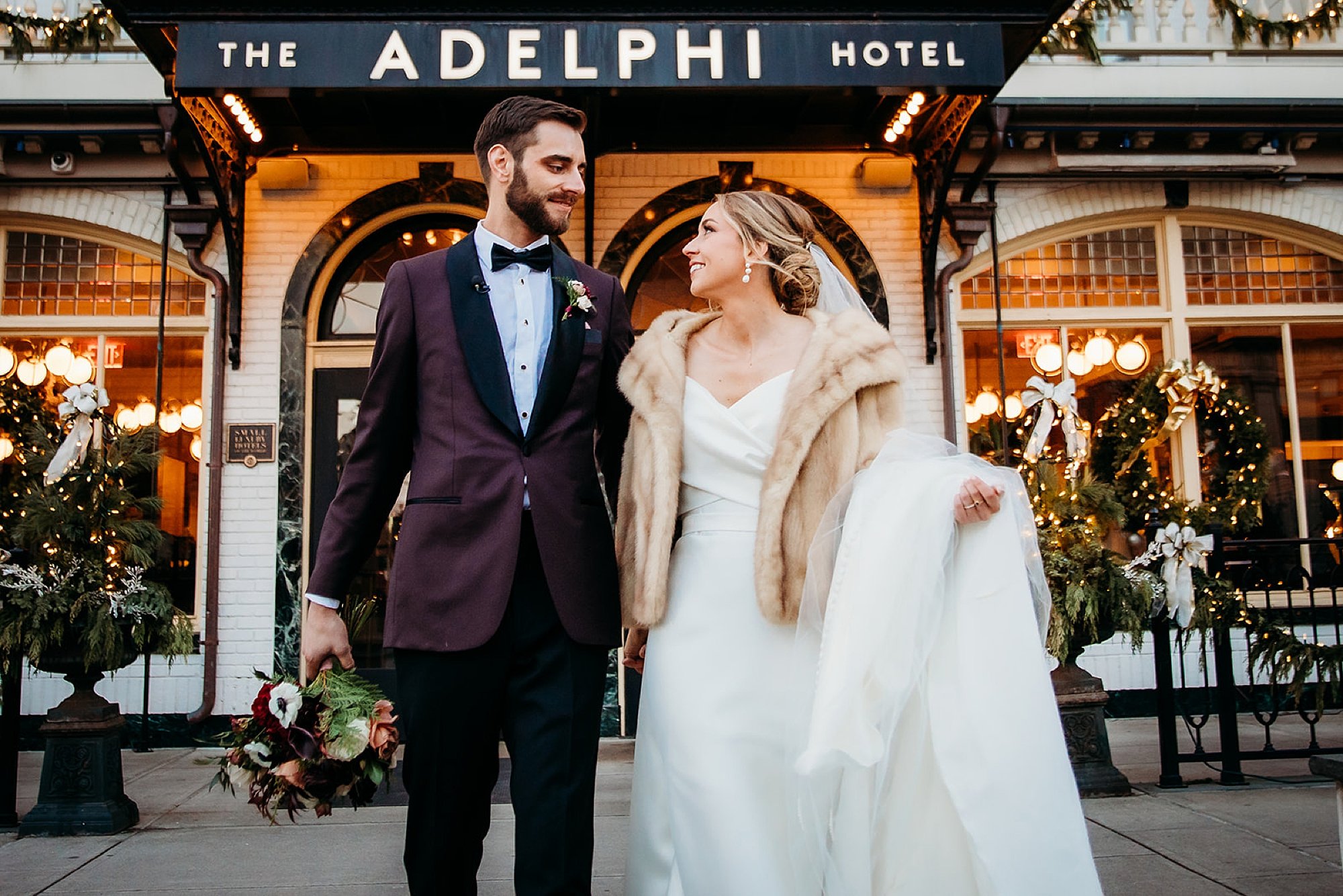 newlyweds hold hands outside The Adelphi Hotel during winter wedding portraits 