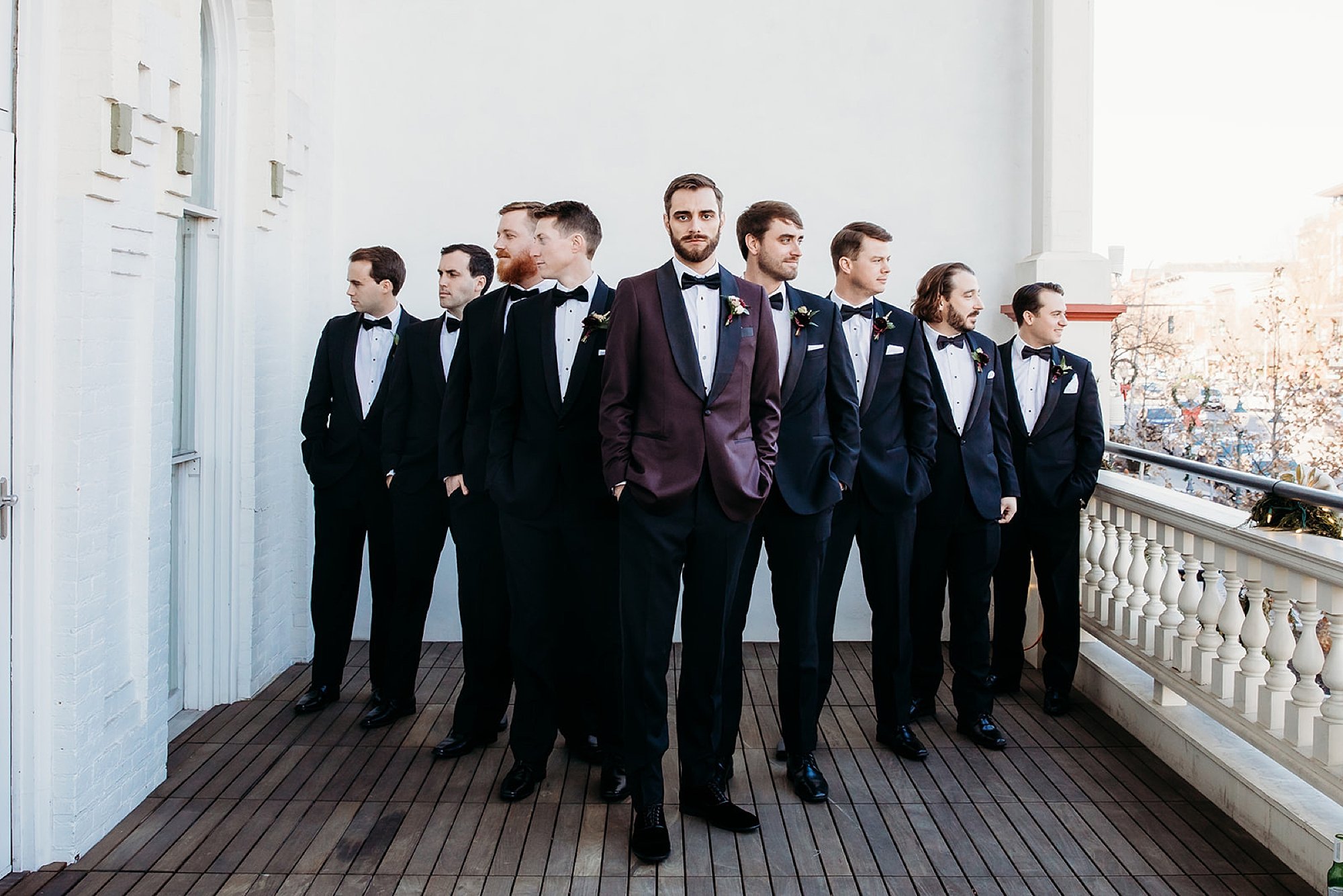 groom stands with groomsmen in burgundy suits on balcony at The Adelphi Hotel