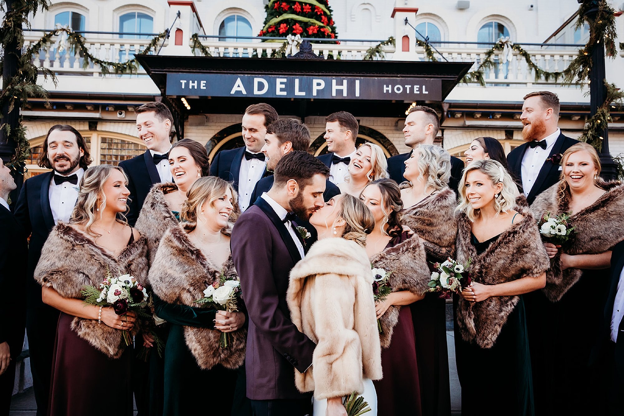 newlyweds kiss with wedding party around them outside of The Adelphi Hotel
