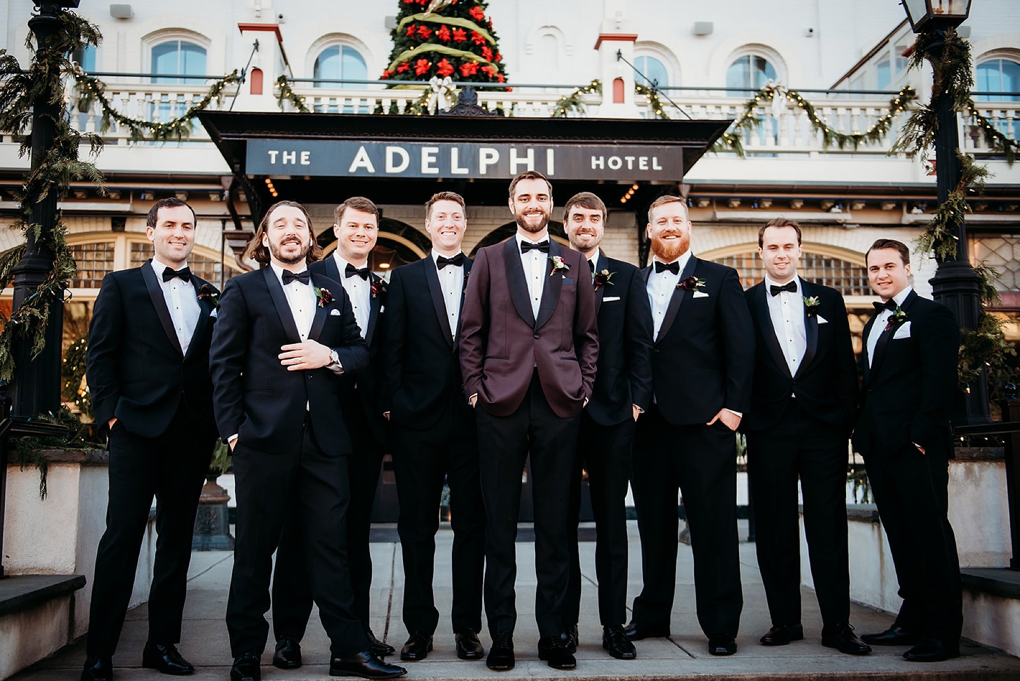 groom stands outside The Adelphi Hotel with groomsmen in black suits