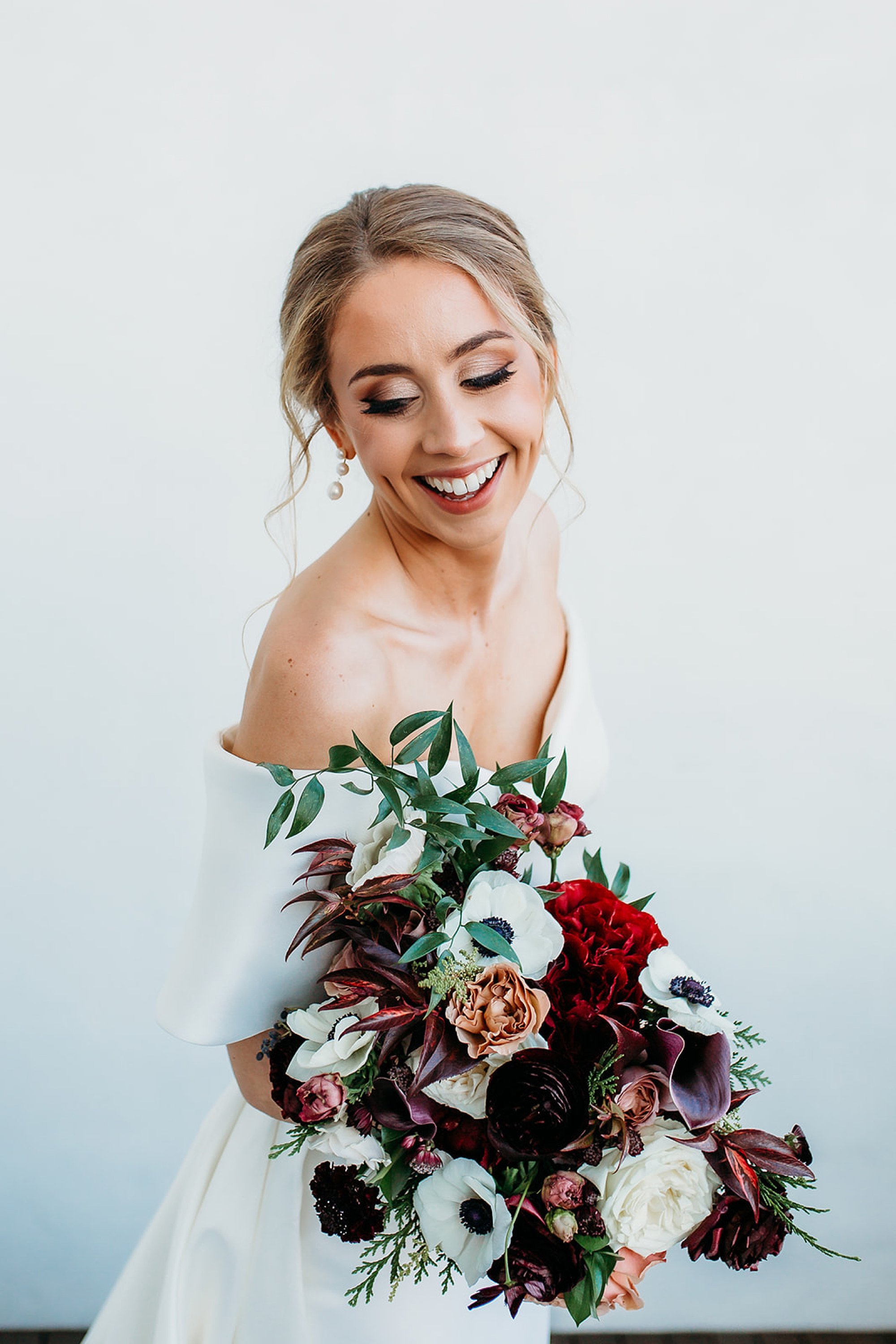 bride holds bouquet in arms laughing over it at The Adelphi Hotel