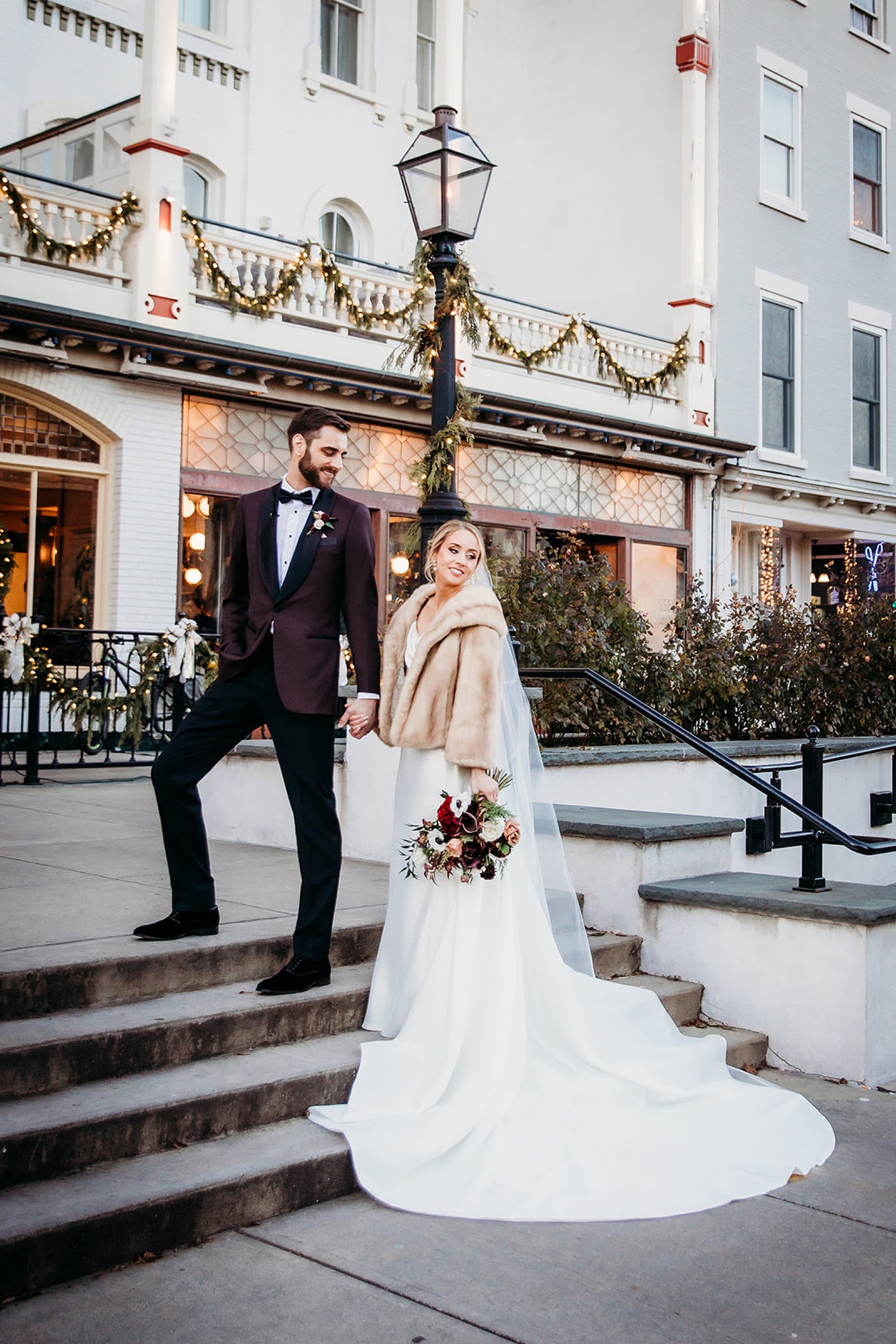 groom in Burgundy suit jacket leads bride up steps outside The Adelphi Hotel