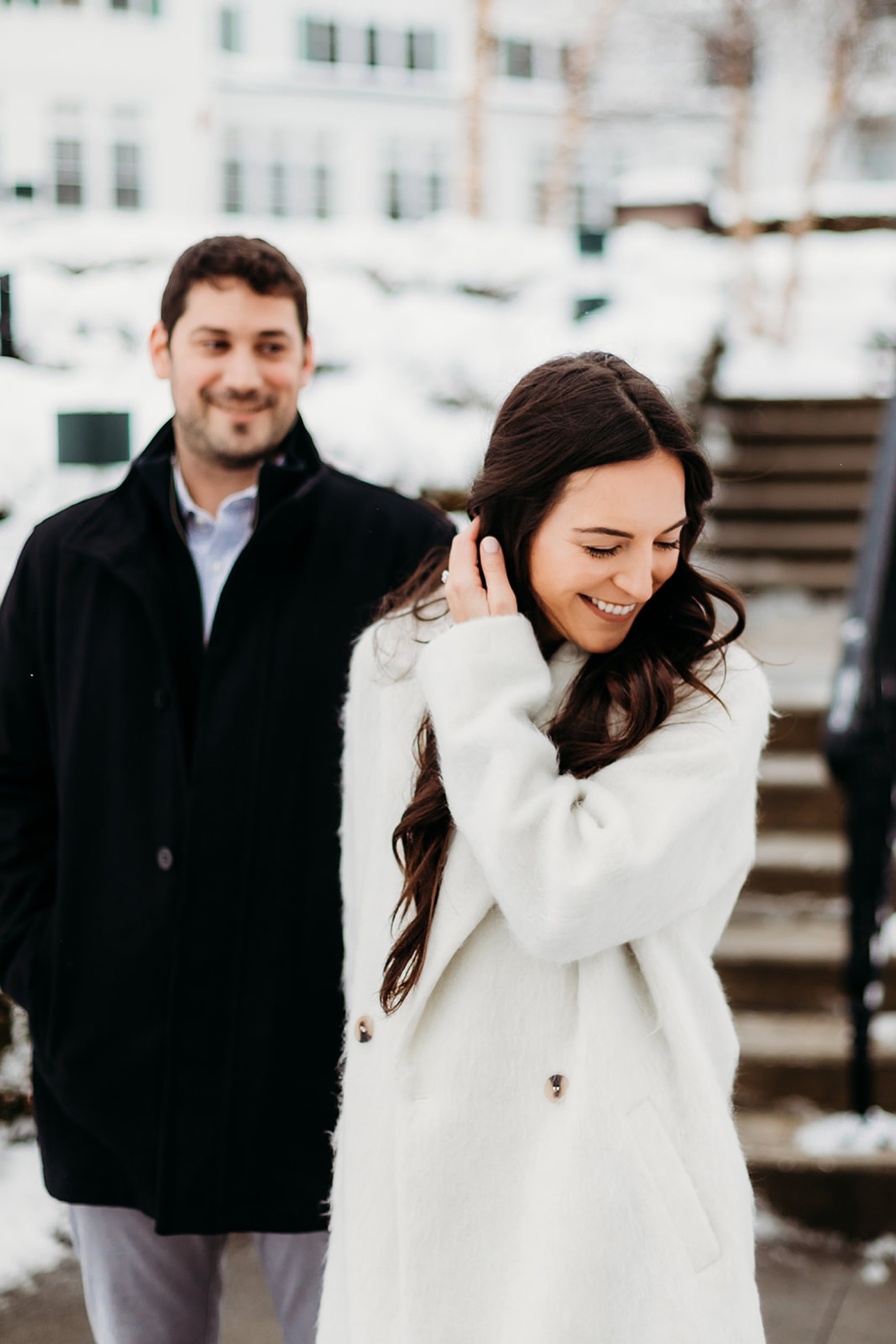 man in black jacket holds woman's hand making her laugh during snowy engagement session at The Sagamore Resort