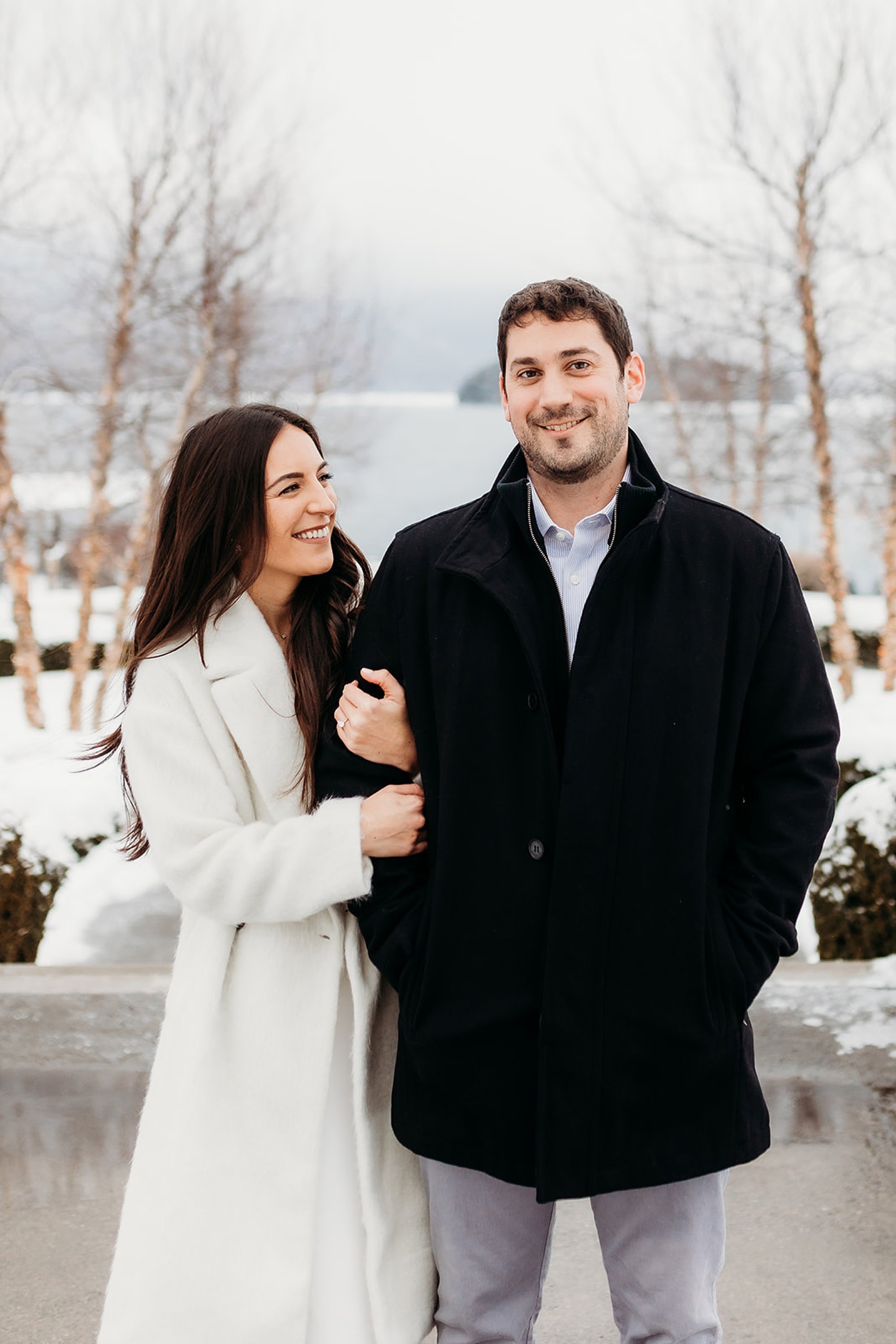 bride holds groom's arm in black jacket during snowy engagement session at The Sagamore Resort